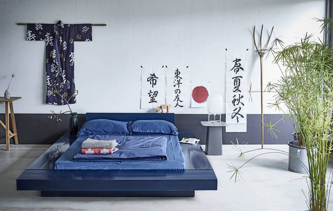 Bed, geschilderd in de kleur Basalt van Little Greene, riek, hoge sidetable links (). Vaasje (). Tweepersoons dekbed Kleon 3, kussens Morfeas, hoeslaken Kalypso 14.1, dekbedovertrek met kussenslopen Elvira 3.1 in indigoblauw ().  van House Doctor in zwart en ivoor,  met wit kruis van De Kussenfabriek, van House Doctor (vtwonen.nl). Lamp Pulpo, bijzettafel van Vitra, houten beer (). Kinderkimono, kalligrafie v.l.n.r. Wens, Aziatische vriend en Vier jaargetijden door Machito Okemoto (). Print Rijzende zon ().