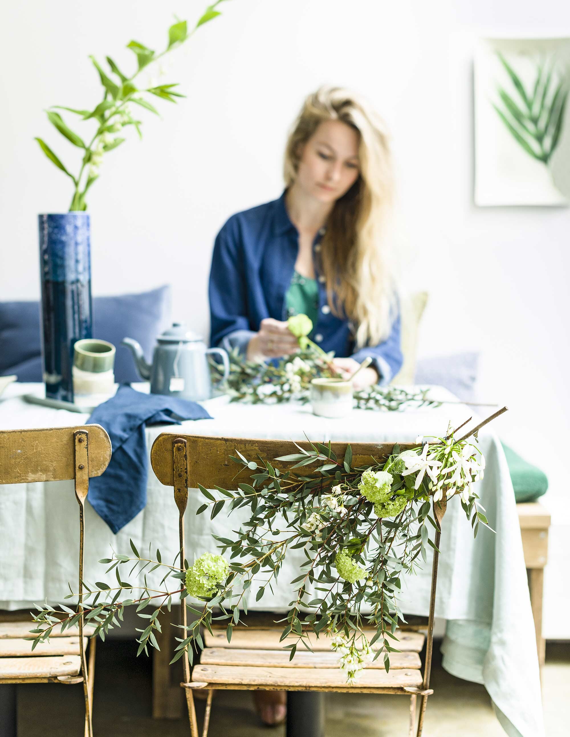 Grote bloem (). Blauwe vaas 35 cm (h), blauwe theepot, bekers (). Denim jurk, lijst met tak (). Lichtblauw tafelkleed 100% linnen, 140×180 cm, blauw servet (). Stof blauw kussen (). Blauw dienblad maat M (). Houten stoeltjes (krinloopwinkel). Boeket (). Houten bank privébezit.