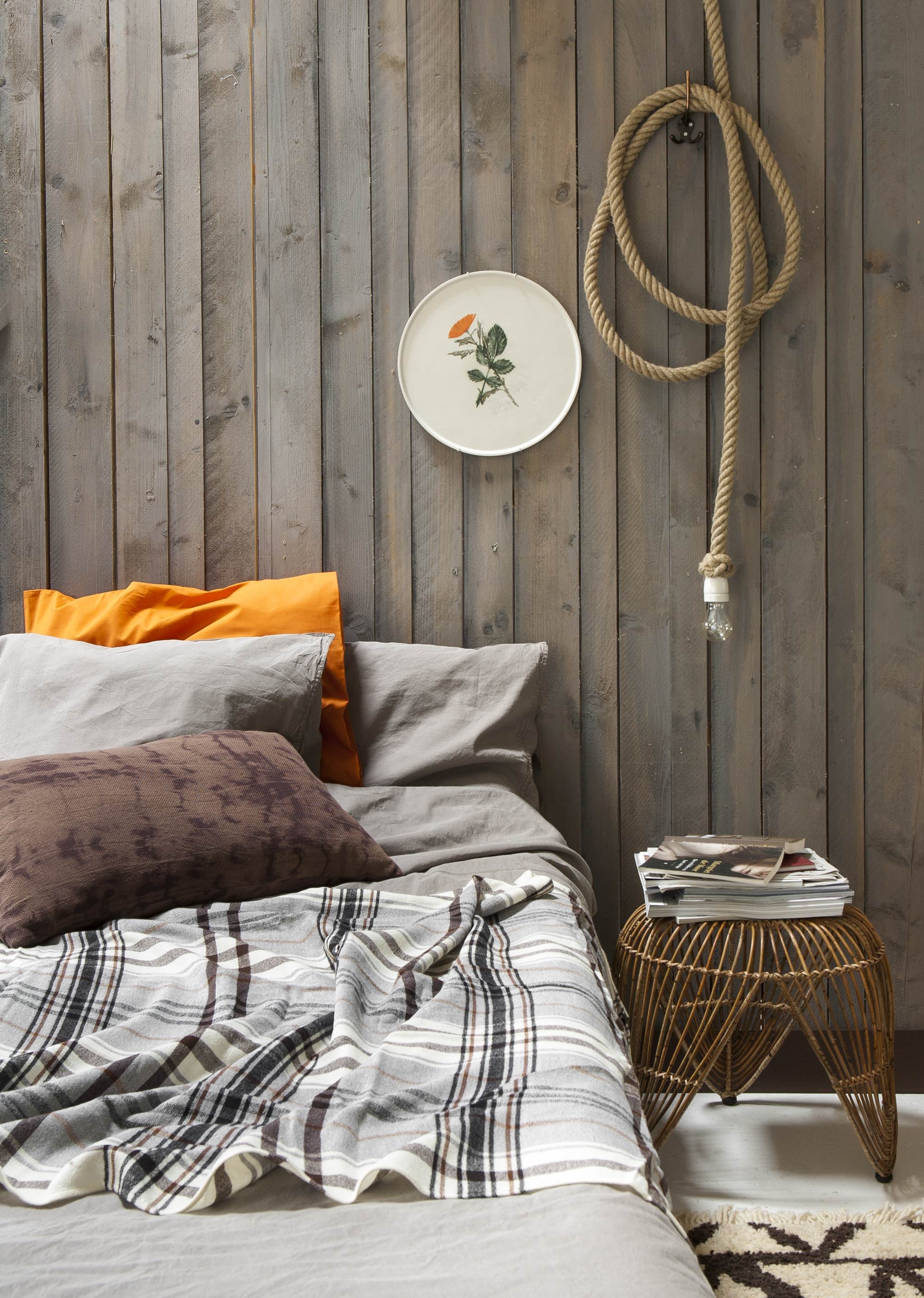 Kruk (L’Etoile Conceptstore). Flax light lamp aan 5 meter touw, ontworpen door Christine Meindertsma, bord Withering tableware, ontworpen door Maarten Kolk en Guus Kusters (Matter of Materials). Dekbedovertrek Momo in kleur Tobacco inclusief 2 slopen (vtwonen.nl). Bruin kussen Indochine Mornings (Loods 5). Oranje kussensloop Dvala, ruiten plaid Hermine (Ikea). Vloerkleed (Friday Next).