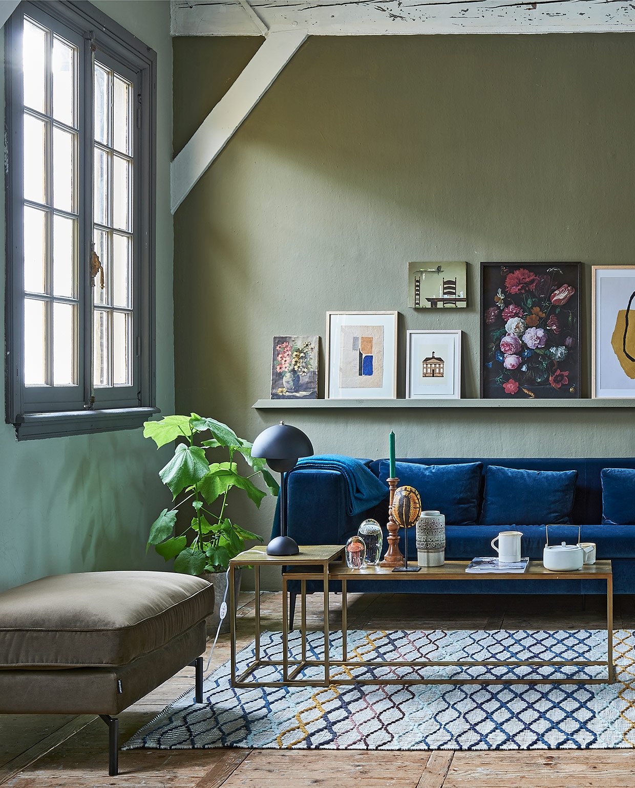 Op de wand muurverf Classico in kleur Tundra (pure-original.com). Bank van blauw velvet , lampje op salontafel (loods5.nl). Salontafel brass, stoel met houten frame, grote blauwe vaas, poef, geborduurd kussen op de bank (polspotten.nl). Zwarte metalen bijzettafel, retro vaas, glazen kwallen, namaak schildpad, theepot (hkliving.nl). Kom, kan, rozenbotteltak XL (weldaad.com). Vloerkleed (ikea.nl). Op de wandlijst: v.l.n.r. schilderij met bloemen (privébezit), grafisch werk (hkliving.nl), illustratie gemeentehuis van Michiel van der Zanden, 30×20 cm (sbk.nl), erboven stoel + tafel (privébezit), print bloemen van het Rijksmuseum (rijksmuseum.nl/nl/rijksstudio), in lijst Hovsta (ikea.nl), grafisch werk (loods5.nl), bloemenschilderij (privébezit). Goudkleurige oude spiegel JA | vtwonen 01-2019 | styling Fietje Bruijn | fotografie Dennis Brandsma