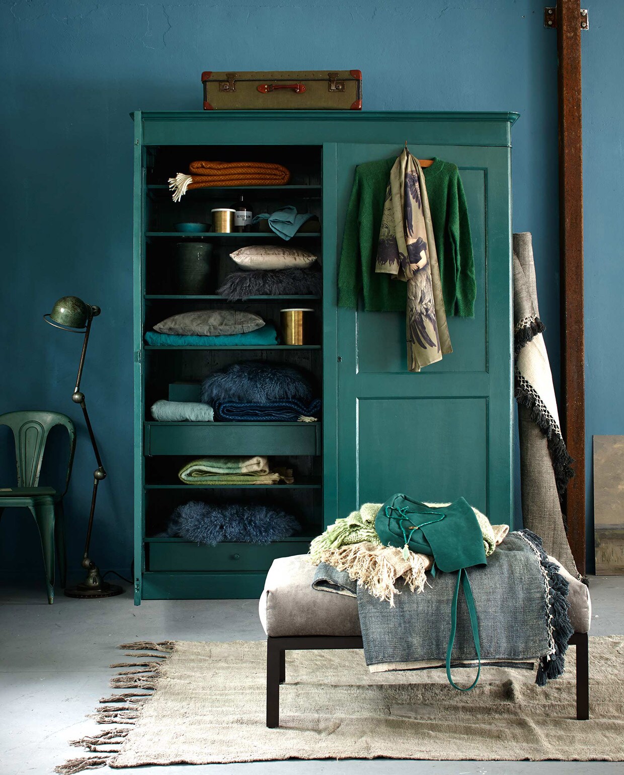 Stoel Forbach, Jieldé lamp Lille koffer (De Weldaad). Kast (Combitex). Vergelijkbare verfkleur: Duizendblad (Histor). In de kast: okergele en blauwe plaid op plank 1 en 5 (Dynamic Comfort). Kom (Serax). Messing pot met marmeren deksel (Madam Stoltz). Apothekersfles (De Weldaad), linnen kussensloop, olijfgroen dekbed (Couleur Locale). Pot (Raw Materials). Beige fluwelen kussen (H&amp;M). Schapenvachtkussens op plank 3 en 5 (Nordal). Grijs canvas kussen (Aai Made With love). Linnen dekbedovertrek (Couleur Locale). Messing pot (Madam Stoltz). Mohair plaid in pastelgroen (De Weldaad). Schapenvacht (Nordal). Aan de deur: trui van Rue Blanche (Sukha Amsterdam). Sjaal (Maison NL). Tegen de kast: vloerkleed (Aai made with love). Poef City bekleed met fluweel (vtwonen.nl). Daarop: ketting, tas (Sukha Amsterdam). Groene plaid (De Weldaad). Beige plaid, grijs vloerkleed (Aai made with love). Vloerkleed 220×135 cm (Raw Materials). Muurverf Pure &amp; Original Classico krijtverf Libo Bay, (De Ru). Overig privébezit.