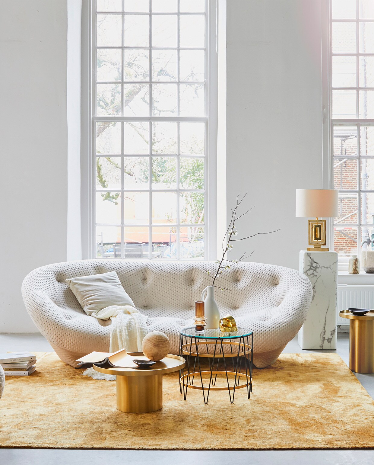 4-zitsbank Ploum van Ligne Roset, 124x84x253 cm (dxhxb) vanaf € 4633,-, okergeel vloerkleed Soft van Jov 260×300 cm € 2738,-, messing bijzettafels, 60×31 cm (Øxh) € 598,-, 43×47 cm (Øxh) € 548,- (misterdesign.nl). Fauteuil Little Petra van &amp;Tradition € 3023,- (mobilia.nl). Bijzettafel met glas en metaal, Ø 50 cm € 550,-, lamp van messing met zijden kap € 750,- (paullelieveld.com). Marmeren pilaar, 33x33x91,4 cm (lxbxh) € 425,-, voetenbankje Pebble € 150,- (polspotten.nl). Linnen plaid € 275,-, okergele vaas € 18,20 (nordal.eu). Grijs fluwelen kussen € 26,50, vaas bladdessin € 27,- (madamstoltz.dk). Zwarte kommen € 25,- (vtwonen.nl). Overig privébezit. JA | vtwonen 02-2019 | styling Cleo Scheulderman | fotografie Jeroen van der Spek