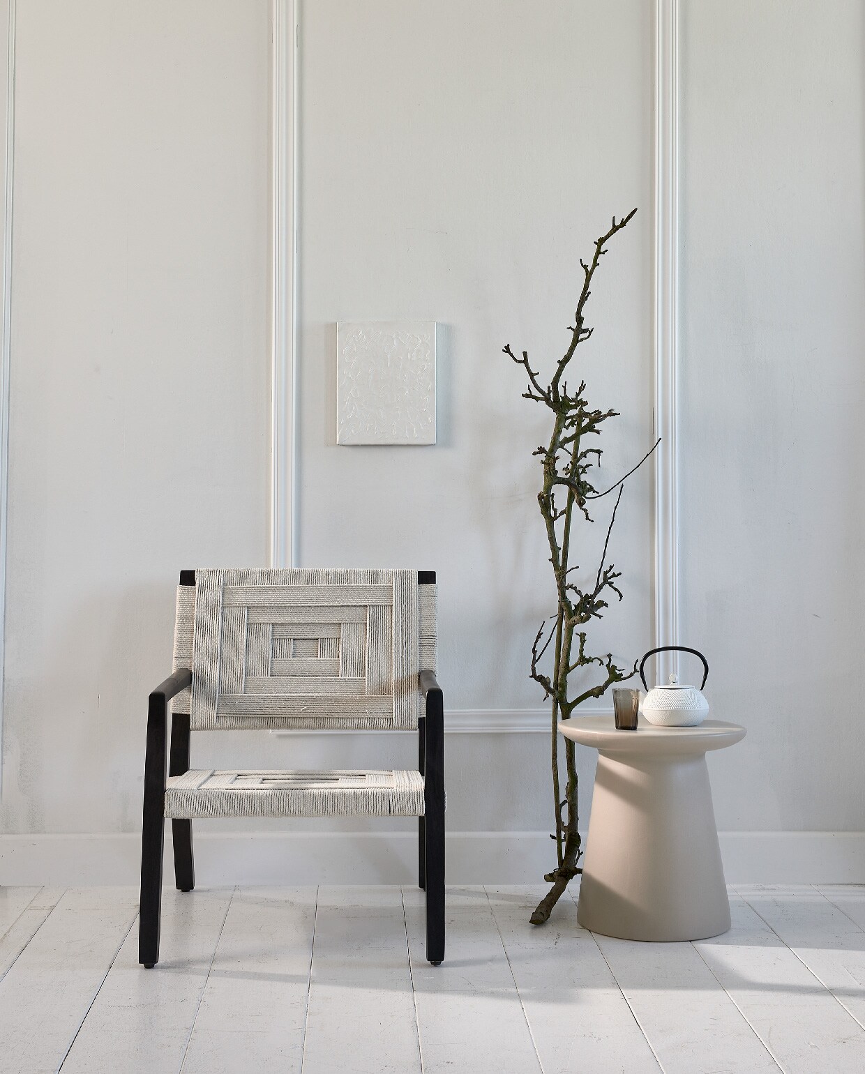 Stoel met gevlochten singels Shima € 272,- (eijerkamp.nl). Keramische tafel € 195,- (hkliving.nl). Japanse theepot € 25,-, grijs geribbeld glas € 3,50 (loods5.nl). Kunst prijs op aanvraag (atolty.com). Lijsten via bouwmarkt.