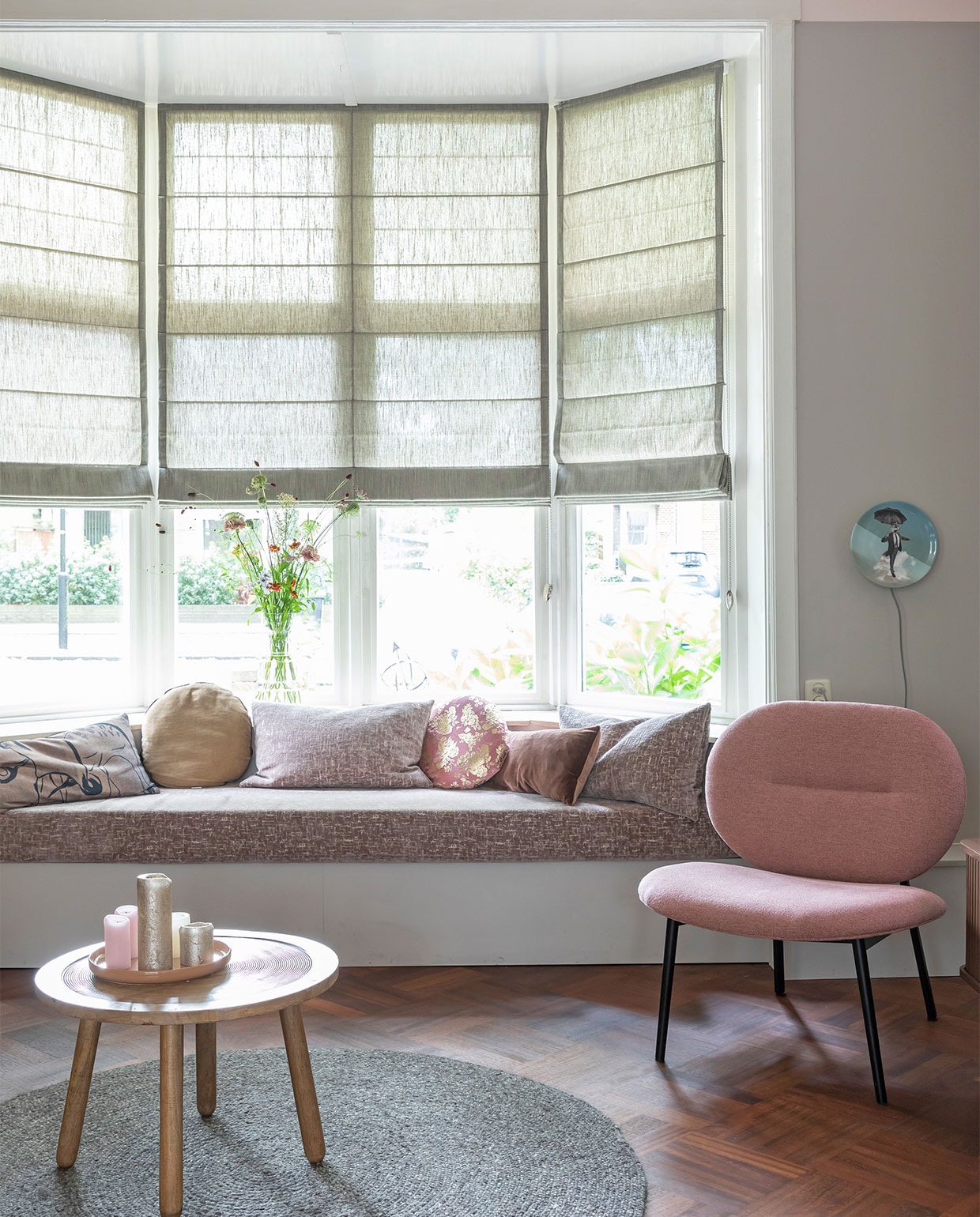 Flexa Creations muurverf op het plafond Stylish Pink, op de muren Urban Taupe (flexa). Raambekleding prijs op aanvraag (woninginrichting-aanhuis). Porseleinen wandlampen van Kikke &amp; Hebbe, per stuk € 179,- (abeltosh.com). Roze fauteuil Spike € 329 roze schaal € 25,90, plaid € 49,95, roze kussen op de bank € 23,95, kussen met rode print van HKliving € 24,95, rond fluwelen kussen € 34,95, roze kussen met gouden print € 36,90, langwerpig kussen € 47,50 (vtwonen.be). Vaas Speckle € 45,- (klevering). Bank en overige kussens in de erker op maat gemaakt.