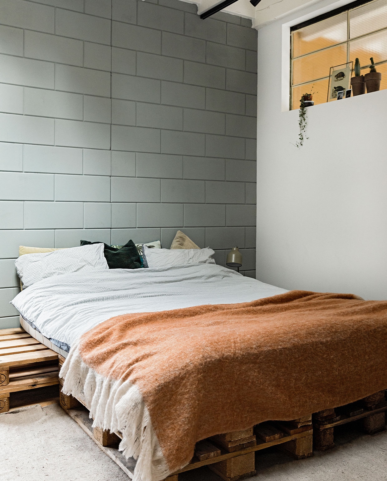 Bed gestapelde pallets, beddengoed Hema, plaid Rivièra Maison. Wandverf kleur Zeegroen van vtwonen. Geverfde leeslamp Hema. Overig onbekend. vtwonen 03-2022 | styling Ilona Jongepier | fotografie Dana van Leeuwen | visagie Djolien de Kreij | tekst Christine van der Hoff