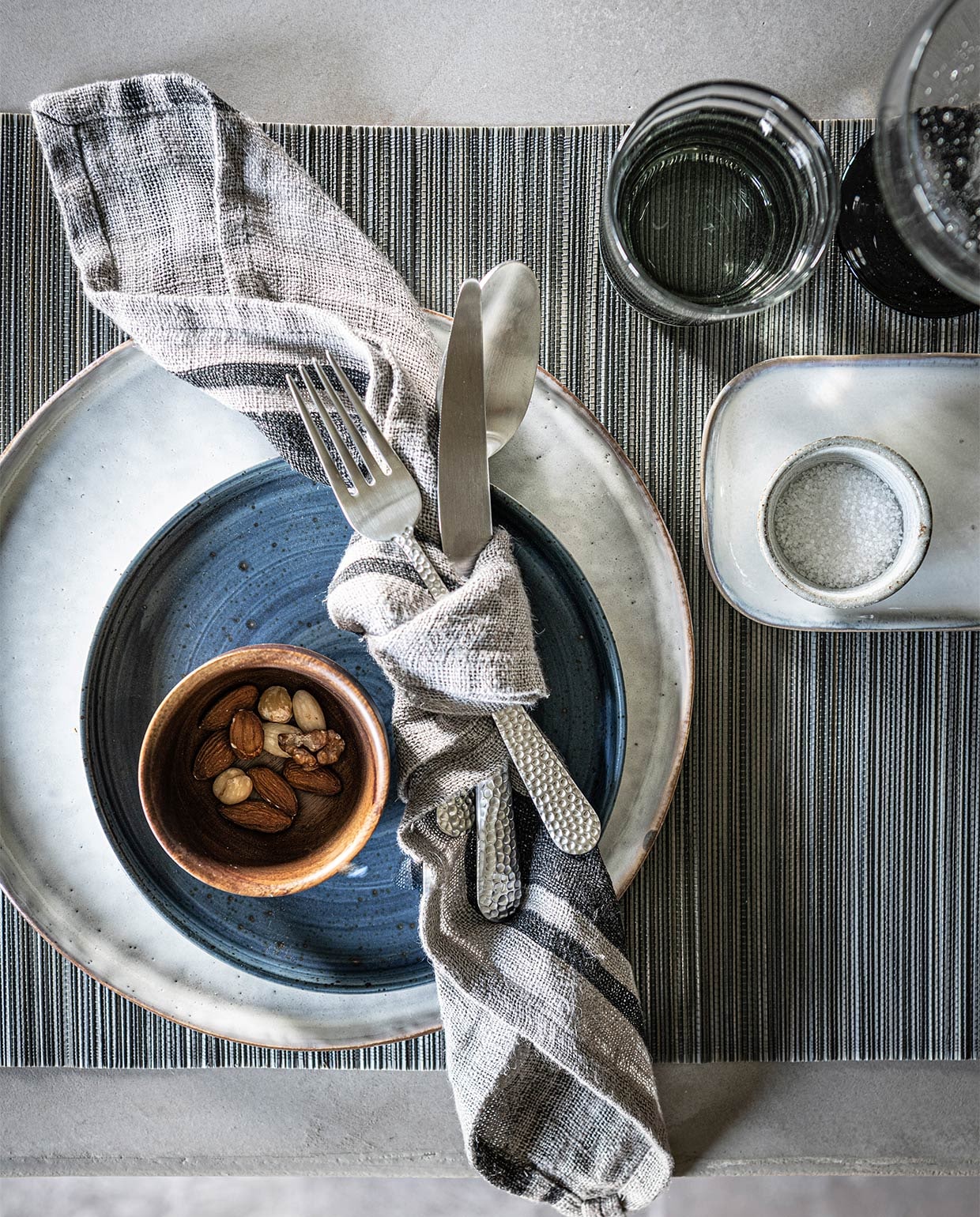 Kom van massief acaciahout van Serax € 13,45 (vtwonen.be). Gehamerd bestek, per stuk € 5,99, bamboe placemat, set van 2 € 6,99 (zarahome.com). Theedoek van HK Living € 11,95, rond grijs bord van HK Living € 14,95, rechthoekig bord van Serax € 19,95 (loftloft). Blauwe bord € 11,95 (letoile.store). Grijs glaswerk vanaf € 8,95 (nordal.eu). Overig privébezit.