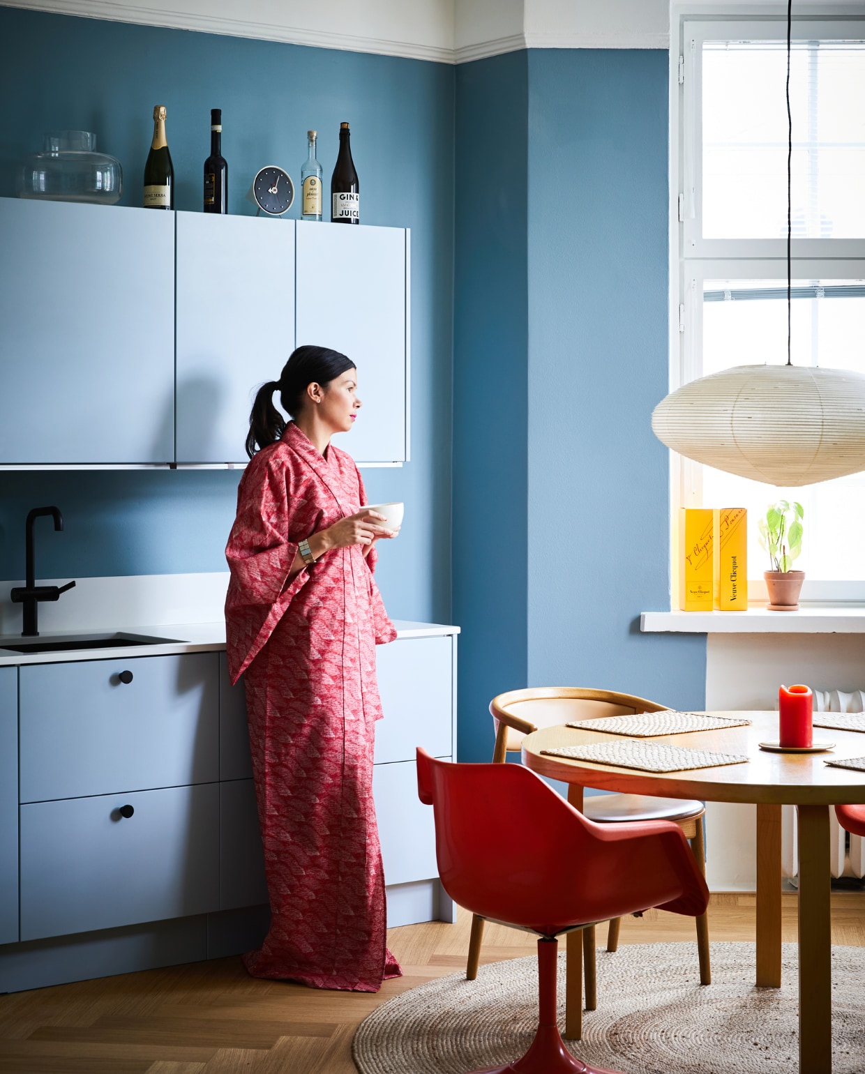 Ook de keuken kreeg een lichtblauwe tint. Eettafel en placemats Artek. Vintage oranje stoel Robin Day voor Hille, houten stoel Mama Hakola. Klok en lamp Akari Vitra. Vloerkleed Anno.