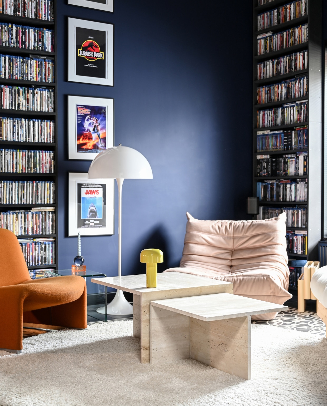 Matte muurverf U2.21.09 Sikkens. Vloerkleed RugVista. Oranje vintagestoel Alky van Artifort. Beige stoel Togo van Ligne Roset. Glazen bijzettafel ted. Amsterdam. Zelf gestapelde, glazen kandelaars Fést Amsterdam. Vloerlamp Panthella van Louis Poulsen. Salontafels Stoned. Draagbare lamp Bellhop van Flos. Vintage lectuurbak Kartell. vtwonen 1-2023 | styling &amp; fotografie Ellis &amp; Michiel