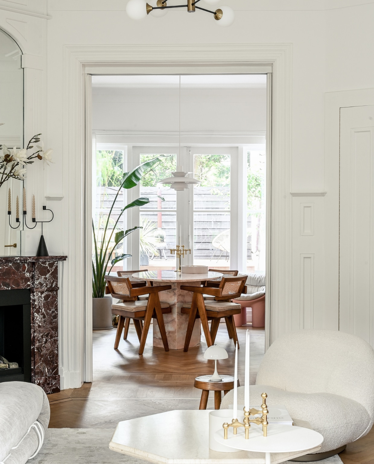 Eettafel en schouw van burgundy-marmer Stoned. Stoelen en houten kruk Detjer. Witte hanglamp PH5 en oplaadbare tafellamp Panthella van Louis Poulsen. Hanglamp met bollen Amazon. Kandelaar op schouw Ferm Living. Fauteuil Gubi. Salontafel vintage. Gouden kandelaar op voorgrond Stoff. Witte bijzettafel &amp;Tradition. Overig onbekend.