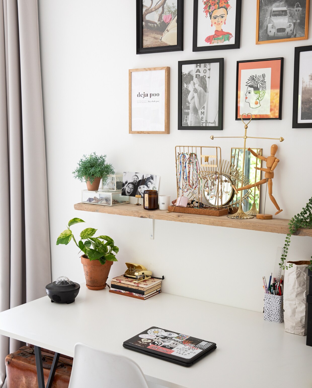 Gordijnen Moondream, muurkleur Ral 9016, lijsten en posters Desenio, foto’s uit tijdschriften, plank Gamma. Op de plank: sieradenhouders uit vintage winkels, spiegels Sissy-Boy, houten tekenpop en planten Xenos. Bureau Ikea, accessoires Hema, stoel Kwantum, koffer van opa.