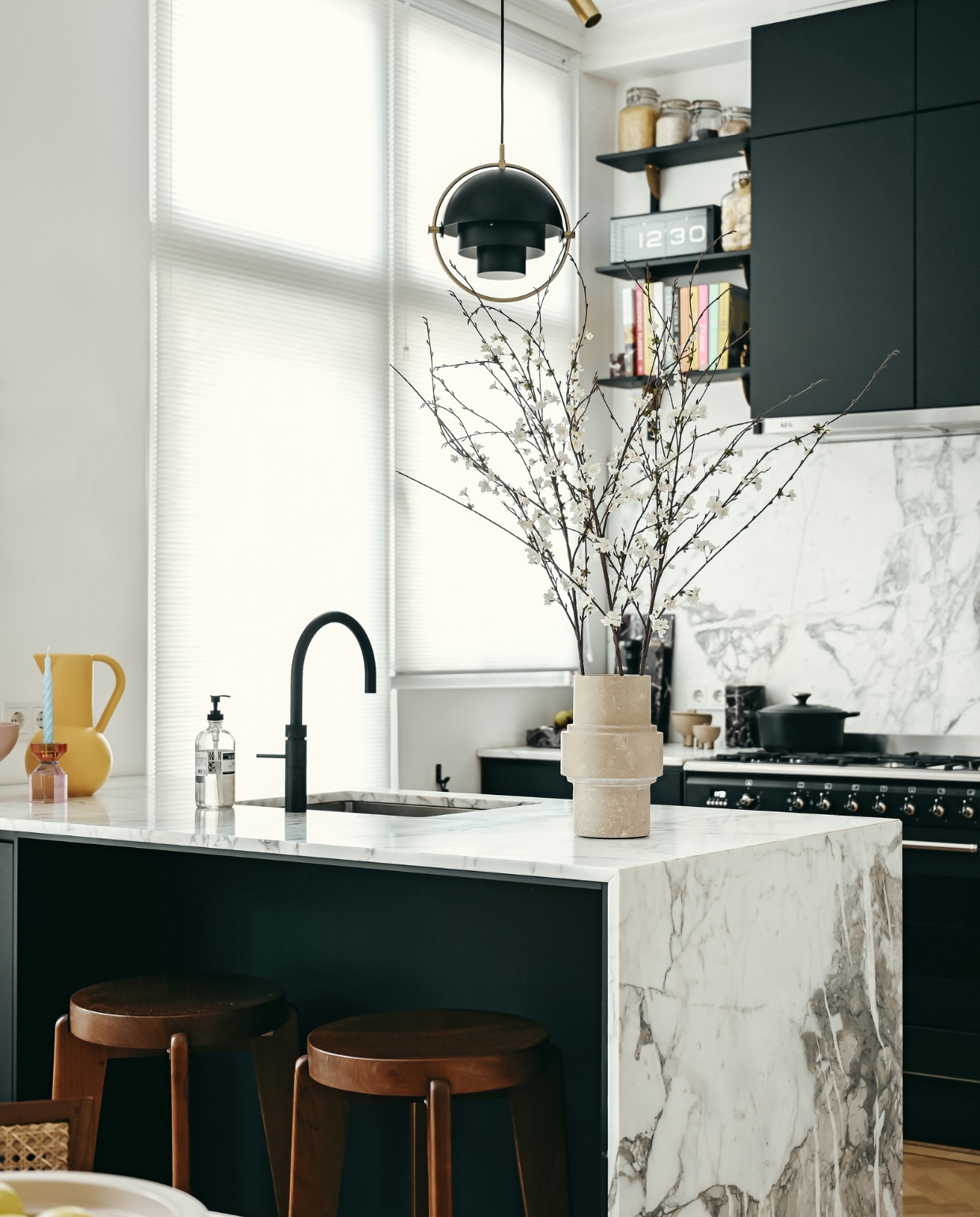 Keukenkasten Kvik, keukenblad en spatwand van Arabscato-marmer Stoned. Kraan Quooker. Barkrukken Detjer. Hanglamp Gubi. Kandelaar Hübsch. Kan raawii. Travertin vaas Column, zwarte, marmeren snijplank en wijnkoeler Stoned. Potjes naast het fornuis 101CPH.