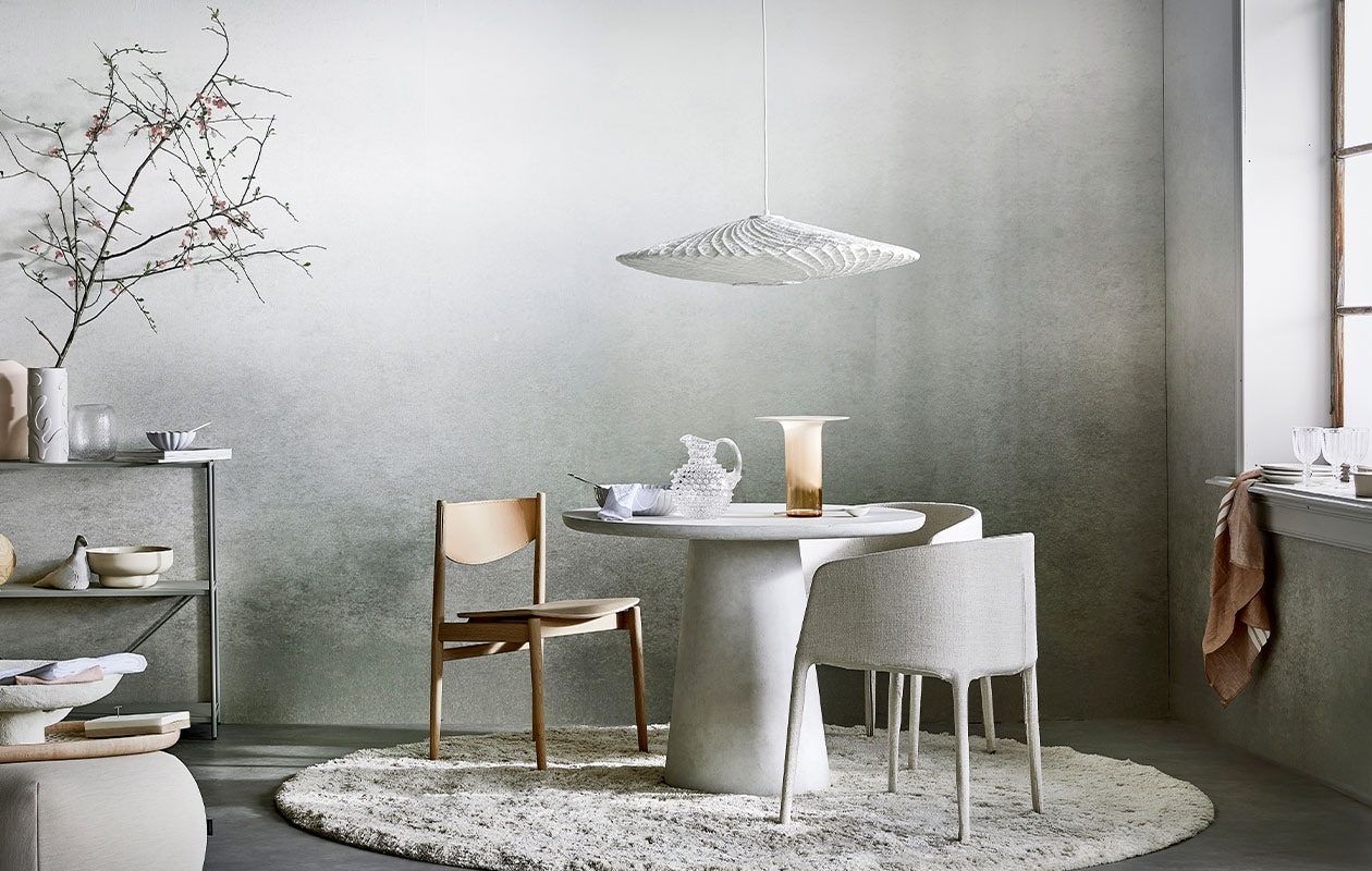 Digitaal behang Degrade Warm Grey, 6 banen van 280×50 cm, totaal (lxb) 280×300 cm € 149,-.M.m.v. loods5.(stellingkast), loods5.nl/design (roze vaas, witte papier-maché schaal, roze schaal), hm.com (witte vaas), bolia.com (glazen vaas, gebroken witte schaal, houten stoel met leren rugleuning), paviljoennoord.com (witte geschulpte schaal klein en groot, wit servet, lepel, glazen kan, roze theedoek, witte borden, wijnglazen), homestede (stoffen vogel, houten dienblad, notitieblok, glazen vaas in koraalkleur), kasstoor (poef, vloerkleed, gestoffeerde eetkamerstoelen, rond vloerkleed), hkliving (hanglamp), basiclabel. (eetttafel Damon), letoile.store (witte porseleinen lepel, theedoek), pure-original.nl (lakverf in kleur Ashes). Overig privébezit.