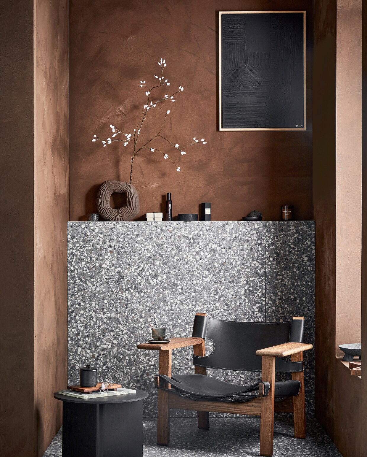 Vloer- en wandtegels Terrazzo Lead Flakes, 90x90 cm per m² € 78,-.M.m.v. vestingh.nl (muurverf Lab Paint in Holy Monkey), designtales.nl (fauteuil van Fredericia), vtwonen.nl (bijzettafel van Hay), boketo.art (kunstwerk), zarahome.com (houten dienblad, zwarte aardewerken pot, onderzetter, zwarte houten schaal), hm.com (aardewerken vaas, glazen bak, ronde houten doos, bruine geurkaars, vierkante houten bak, zwarte aardewerken schaal op poten, houten dienblad in organische vorm). Overig privébezit. vtwonen 02 2023 | productie Tanja Saarberg | styling Sanne Ketelaar | fotografie Peggy Janssen