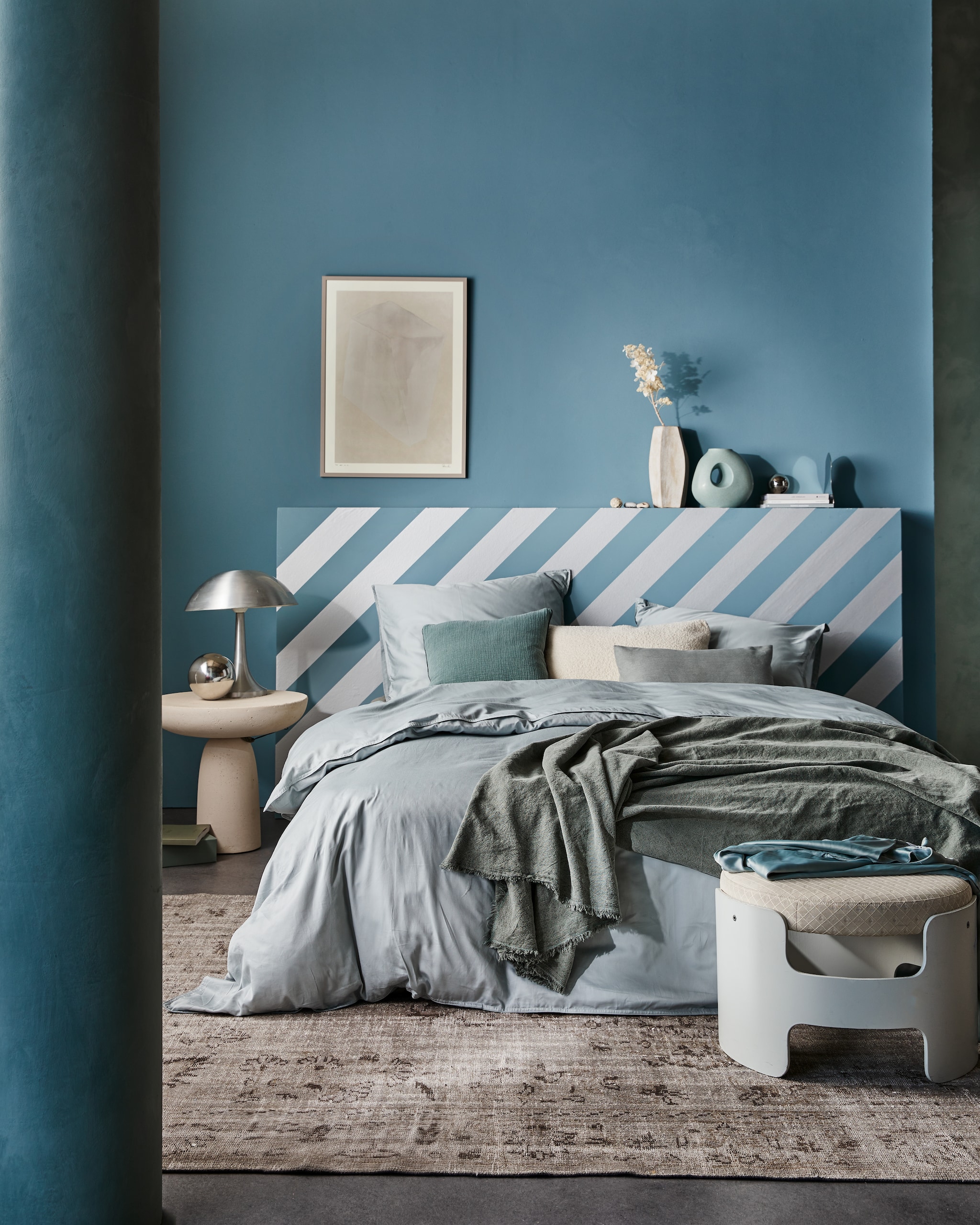vtwonen collectie behangstrook Silver, 10,66 cm (b), rol van 10 m € 12,99. M.m.v. suite702.nl (satijnen beddengoed in Glacier Grey), neeflouis.nl (poef), edha-interieur.nl (bijzettafel), pietjonker.nl (zilveren lamp), urbannatureculture.com (vazen), rozenkelim.nl (vloerkleed), theposterclub.com (ingelijste poster), zarahome.com (linnen plaid, kussens), vtwonen.be (muurverf in Old Blue). Overig privébezit. productie Tanja Saarberg | styling Cleo Scheulderman | fotografie Jeroen van der Spek | assistentie Kelly van Gendt | studio en decorbouw Studio Milo