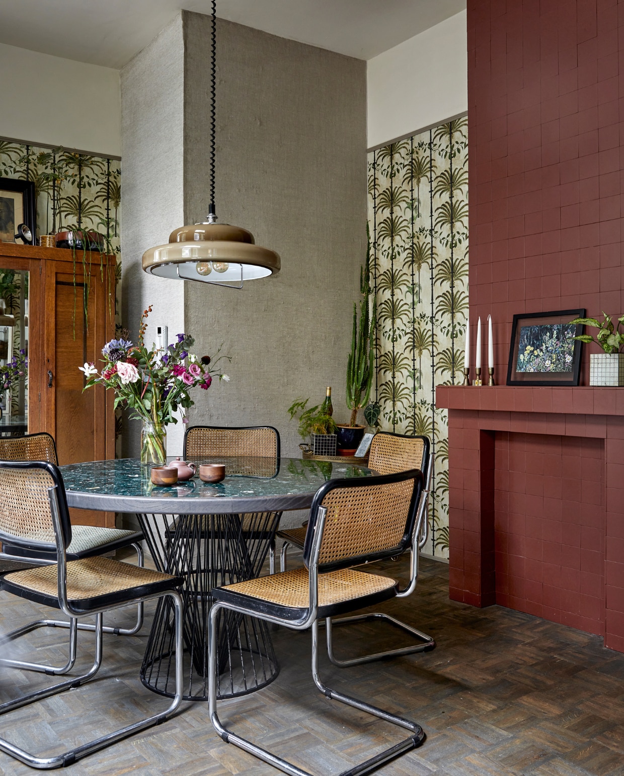Behang Havana Taupe van Mind the Gap. Tegels haard Winckelmans in kleur Rouge. Tafel met terrazzoblad eigen ontwerp Buroboro. Theepot relatiegeschenk, kopjes Serax. Hanglamp gevonden op straat. Stoelen en kast Marktplaats. Plantenpotten Serax. Ingelijste print op schouw van schilderij gemaakt door Rosans oma. Kandelaars Xenos. Bijzettafel van Bo’s moeder geweest. vtwonen special binnenkijken 2022-3 | Fotografie Peggy Janssen | Tekst Caroline Westdijk