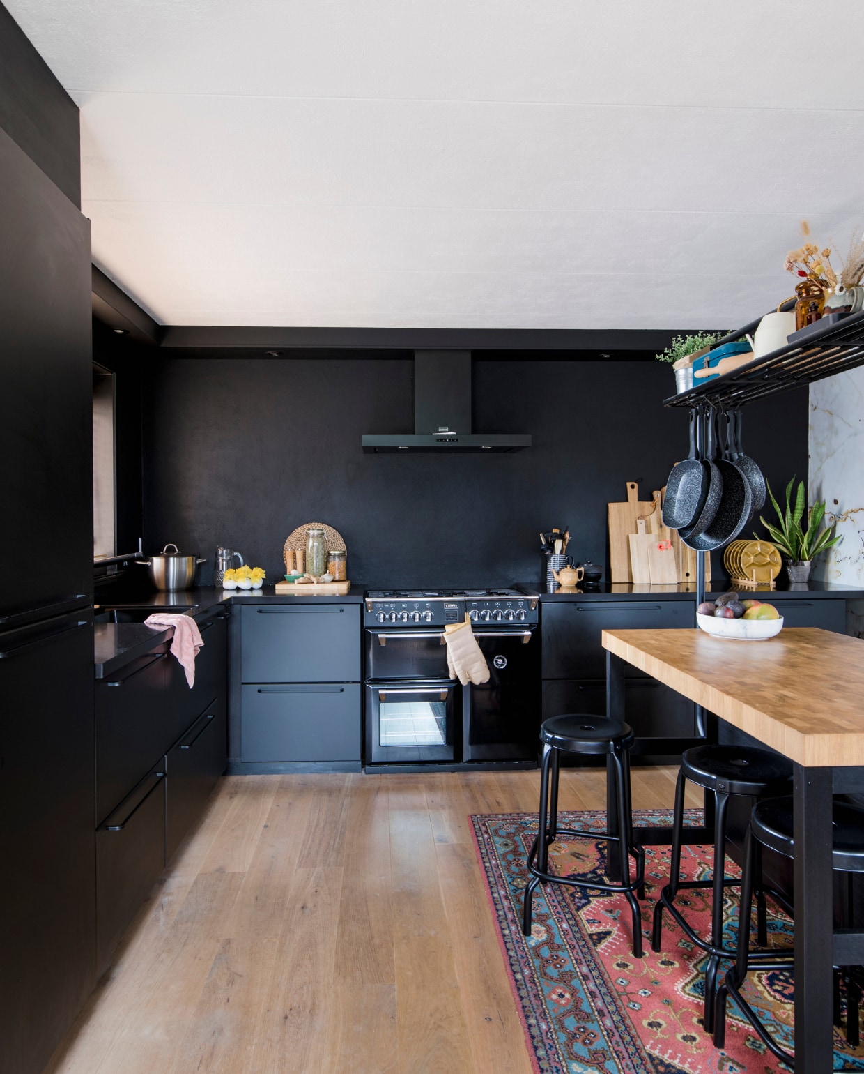 Keuken, hoge tafel en krukken Ikea. Fornuis en afzuigkap Stoves. Karpet en blauwe emaillen beschuittrommel familiestukken. Okergele borden kringloopwinkel. Zwarte theepot Bredemeijer. Snijplanken van Broodt, Xenos, Hema en Ikea. Fruitschaal Bowls and Dishes, hangende pannen Blokker. vtwonen 12-2022 | fotografie Corine Hoge Bavel | tekst Chris Muyres