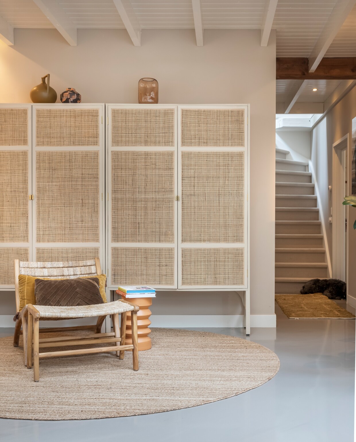 Muurverf Mushroom van Little Greene, verf plafond RAL 9010, vloer gietvloer. Kasten HKliving. Vazen op kasten van links naar rechts: HKliving en laatste H&amp;M. Stoel HKliving, kussens op stoel HKliving en Loods 5. Bijzettafel, rond vloerkleed en kleed voor trap HKliving. Overig onbekend. vtwonen 02-2023 | styling Karin van Schie | fotografie Henny van Belkom