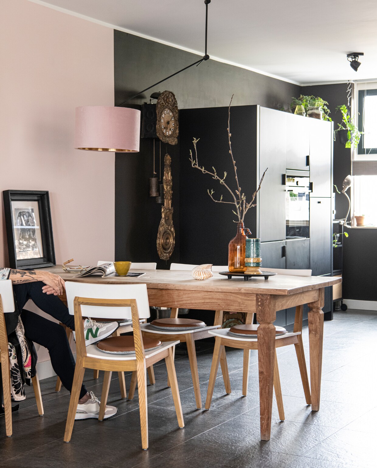 Muurverf Stylish Pink en Fading Horizon van Flexa, eettafel en eetkamerstoelen tweedehands, lamp van Rietveldlicht, bruine flesvaas en vaas kringloop, klok antiek, portret van Nera door Renee Klein, keuken zwart laten spuiten door Spuiterij Rood. Overig onbekend. vtwonen 01-2023 | Productie Inside Homepage | Fotografie Louis Lemaire | Styling Anja Bas Backer