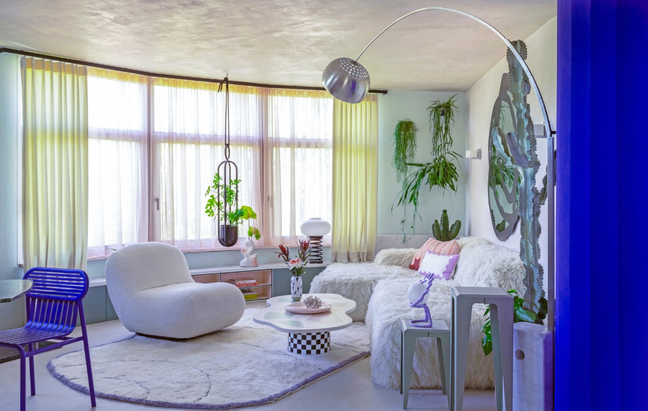 Gordijnen Ado Goldkante. Lage wandkast op maat gemaakt. Organische vaas Hannah Simpson Studio. Spiraallamp vintage. Plantenhanger Atelier Haussmann. Blauwe stoel Petite Friture. Fauteuil Chelsea BoConcept. Vloerkleed eigen ontwerp, handgemaakt in Marokko. Op maat gemaakte salontafel Minerva Artlab. Vaas Studio Arhoj. Roze bord Moustache. Bank Pyllow Mycs, schapenwollen bekleding zelfgemaakt. Bijzettafels Chamfer Wye Design. Paarse oog-lamp mattina moderna. Vloerlamp Arco Flos. vtwonen binnenkijken special 121-2022 | productie, fotografie &amp; tekst Anne Catherine Scoffoni | tekstbewerking Caroline Westdijk