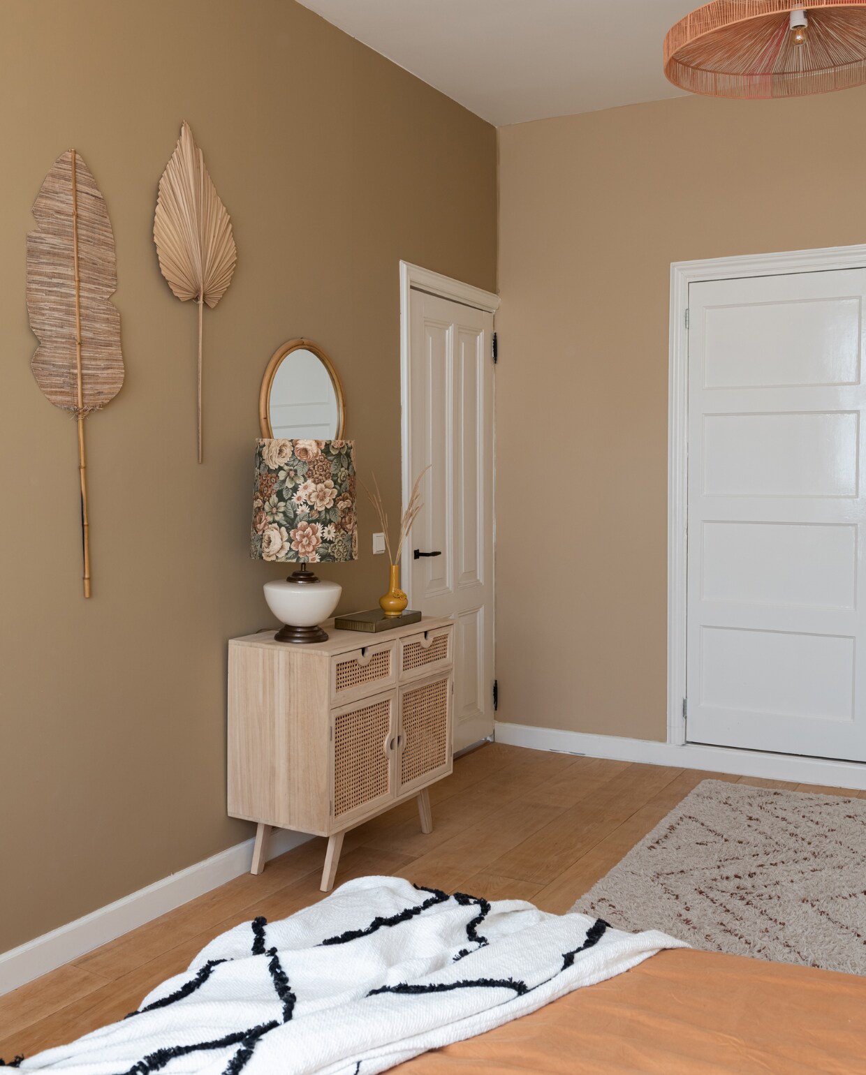 Muurkleur bruin Natural en beige Calm van Praxis. Muurbladeren Kwantum, spiegel Leen Bakker, hanglamp Rope van HKliving. Kast Sklum, tafellamp kringloopwinkel, vaas Shopbywoon, sprei Karwei, beddengoed H&amp;M Home, vloerkleed en bed Wehkamp Home. vtwonen 02-2023 | Styling Sharon Roest | Fotografie Caroline Martinot | Tekst Mirjam Rosema-Verhulst