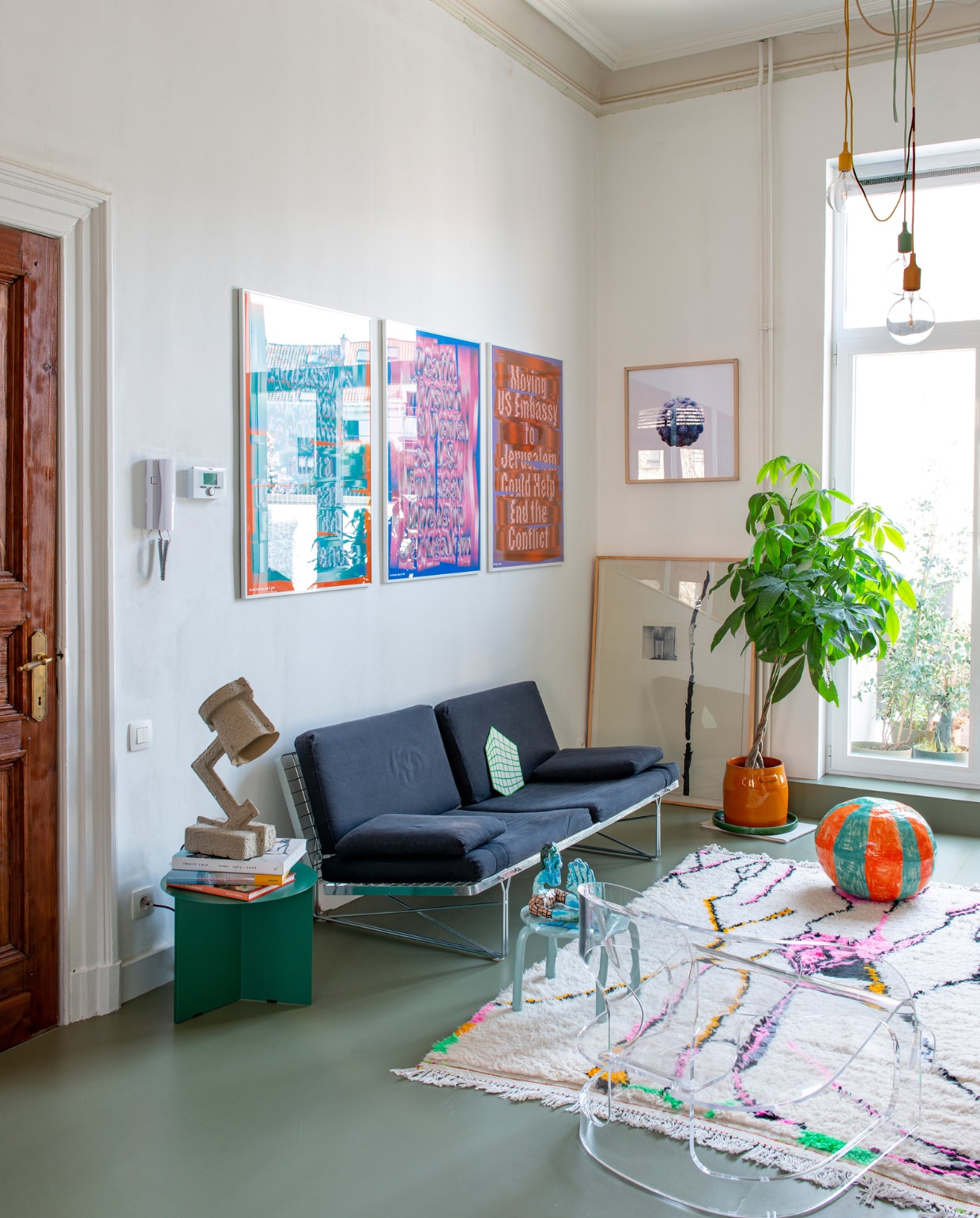 Zeefdrukken Truth’s Triptych van Ward Goes, zeefdruk ernaast Coen Pausma, op de vloer kunstwerk Shelagh Keeley, bank Moment van Niels Gammelgaard voor Ikea, papier-maché lamp Trash Me van &amp;Tradition, groene bijzettafel Slit van Hay, blauwe bijzettafel Sarah &amp; Charles voor Artlead, daarop papier-maché mannetje van Popermacho, transparante fauteuil Joe Colombo voor Kartell, vloerkleed Petit Maroc, bloempot Serax, keramische strandbal Polly Huyghe, hanglampen E27 van Muuto. vtwonen 02-2023 | styling: Jeske Weel | fotografie: Caroline Coehorst