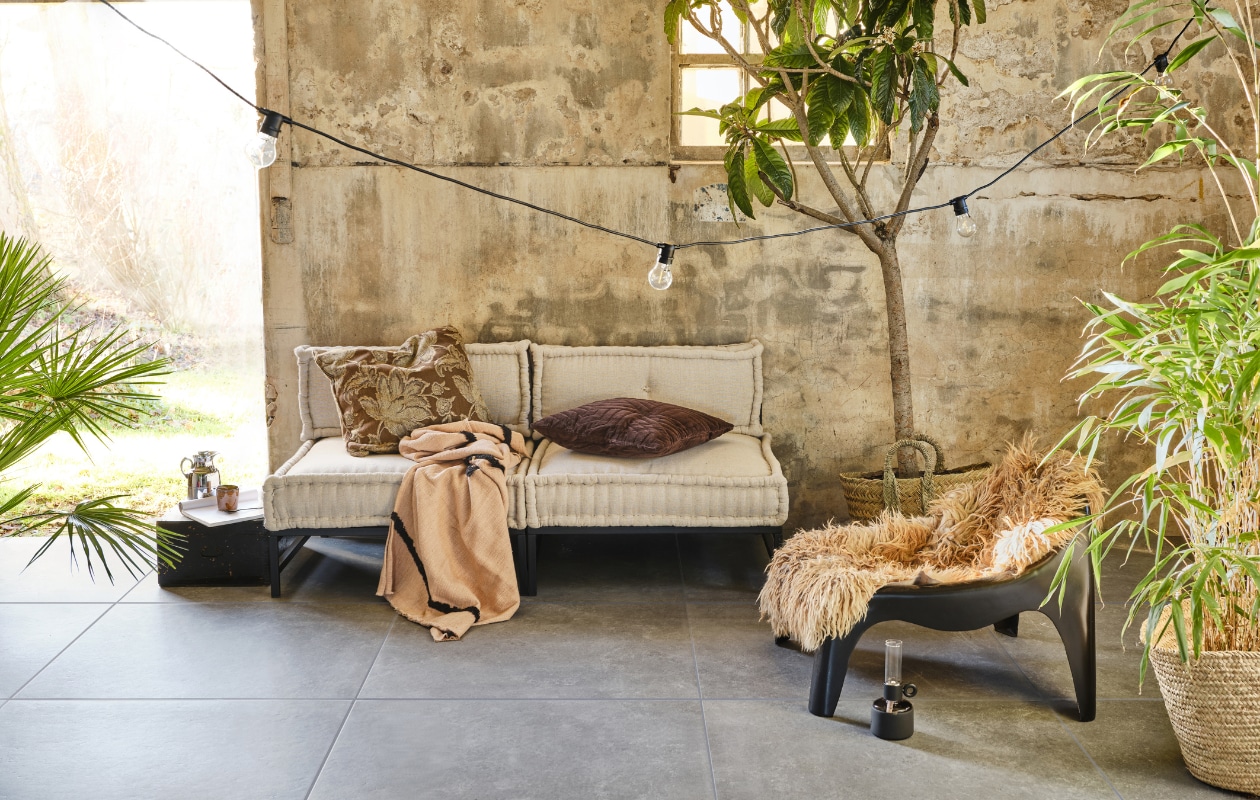 Tuintegel Unico Antracite, 90x90 cm per m² € 89,50 (ook in de kleur Sand). M.m.v. householdhardware.nl (bank bestaande uit losse elementen, kunststof fauteuil, rieten manden), vtwonen.nl (plaid van HKliving, mok en lichtsnoer van Serax, bruin velvet kussen, lantaarn van Fatboy), com-anders.nl (kussen met print), jolandelijk.nl (opbergkist, thermoskan). Overig privébezit. vtwonen 03-2023 | productie Tanja Saarberg | styling Marlies Does | fotografie Bart Brussee