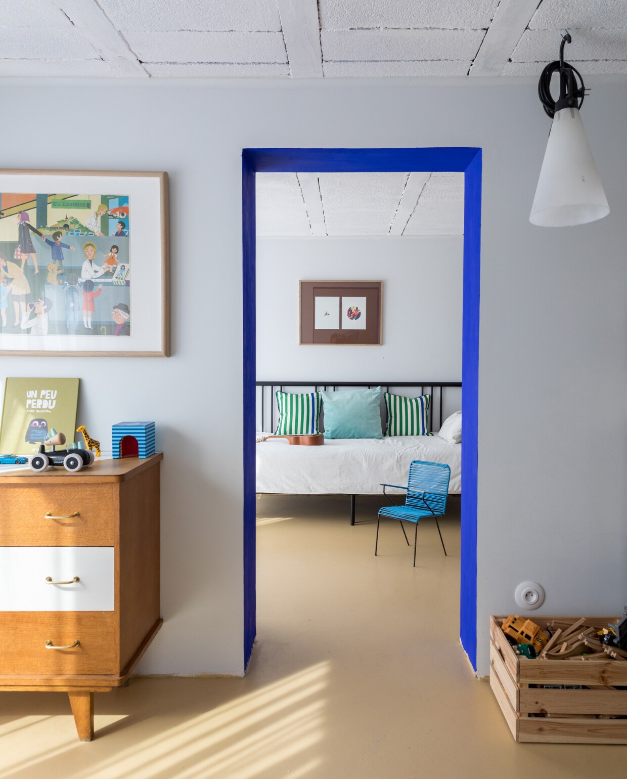 Vloer geverfd in Beige Tadrart van La Seigneurie, kozijn in Yves Klein Blue van Resources. Bed Ikea en vintage ladekast via leboncoin.fr. Gestreepte kussens Monoprix. Effen kussen Élitis. Sprei Maison de Vacances. Vintage Scoubidou-stoeltje vlooienmarkt. Lamp Mayday Flos. vtwonen special binnenkijken 11-2022 | productie &amp; styling Marie Maud Levron | fotografie Cecile Perrinet-Lhermitte