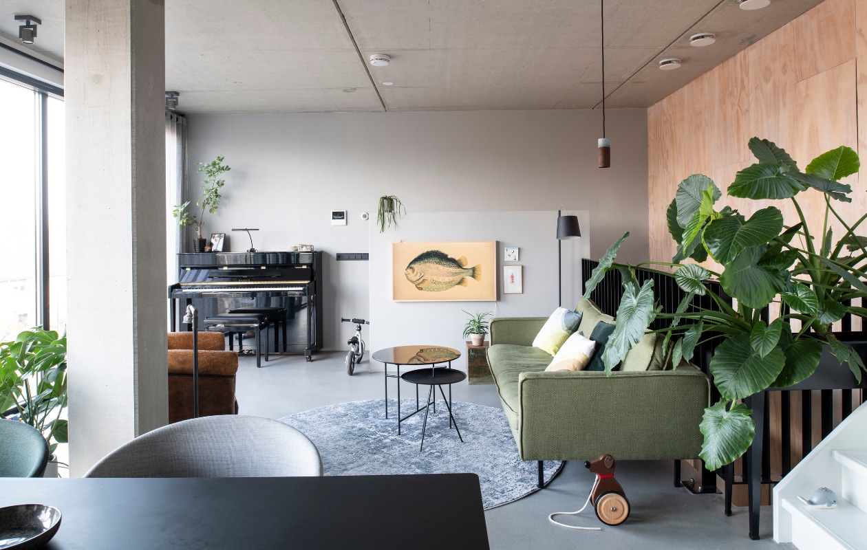 In de woonkamer op de tweede verdieping ligt Pandomo K3 stuc als variant op een gietvloer. Zetel Loods 5 Design. Herringbone kussens van Vitra via Groen + Akker. Groen kussen en plantenstandaard Intratuin. Vloerkleed Gusta. Hoge bijzettafel Loods 5. Lage bijzettafel Woood. Vloerlamp Zuiver. Hanglamp Roest van Van Joost voor Graypants. TV Samsung Frame met camouflagebeeld vis. Tegel StoryTiles. Schilderij gekocht in een Parijse galerie. vtwonen 11-2021 | productie Insidehomepage | styling Inge van Lieshout | fotografie Louis Lemaire