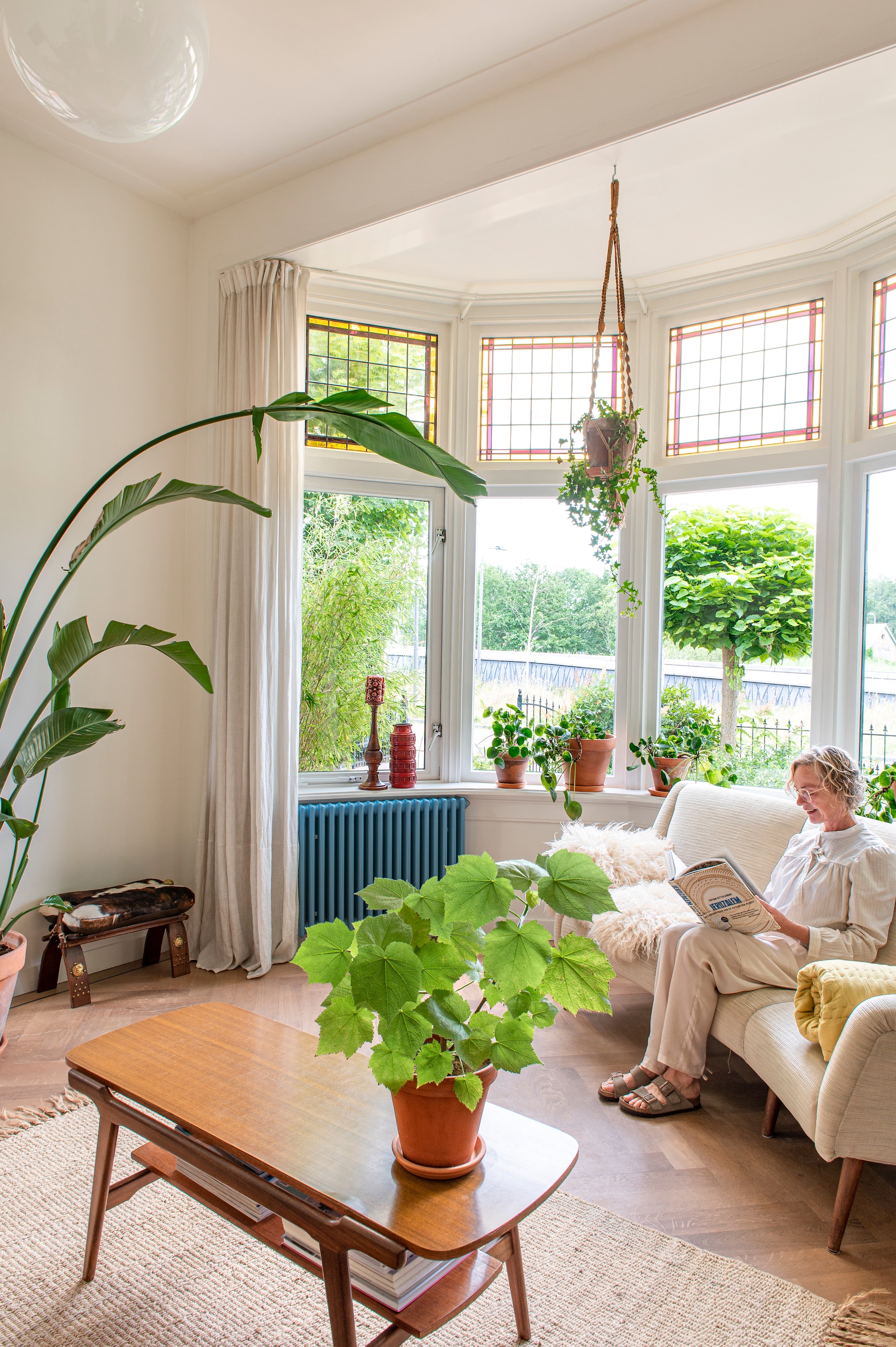 De eikenhouten visgraatvloer lag al in het huis. Verfkleur muur RAL9010. Linnen gordijnen Ikea. Salontafel Louis van Teeffelen. Bank Marktplaats. Gele plaid Loft. Vacht uit Frankrijk. Koeienbank rommelmarkt. Kandelaar en vaas Vanouds. Planten en plantenpotten De Blaakhof. Radiator Zehnder Charleston in kleur RAL5024. Glas in lood verduurzaamd door Van der Staaij ambachtelijke restauratie. vtwonen 03-2023 | Styling en fotografie Caroline Coehorst i.s.m. Studio Daan Hietbrink