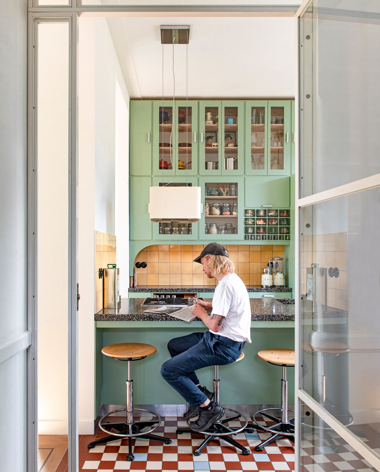 Glazen deuren Goedezaak. Keuken ontworpen door Studi Daan Hietbrink, verkleer fronten Room Green 81 van Farrow &amp; Ball. Keukenblad Marcolina Terrazzo en Beton. Wandtegels en barkrukken Marktplaats. Vloertegels Winckelmans. Blender en melkschuimer Smeg. vtwonen 03-2023 | Styling en fotografie Caroline Coehorst i.s.m. Studio Daan Hietbrink