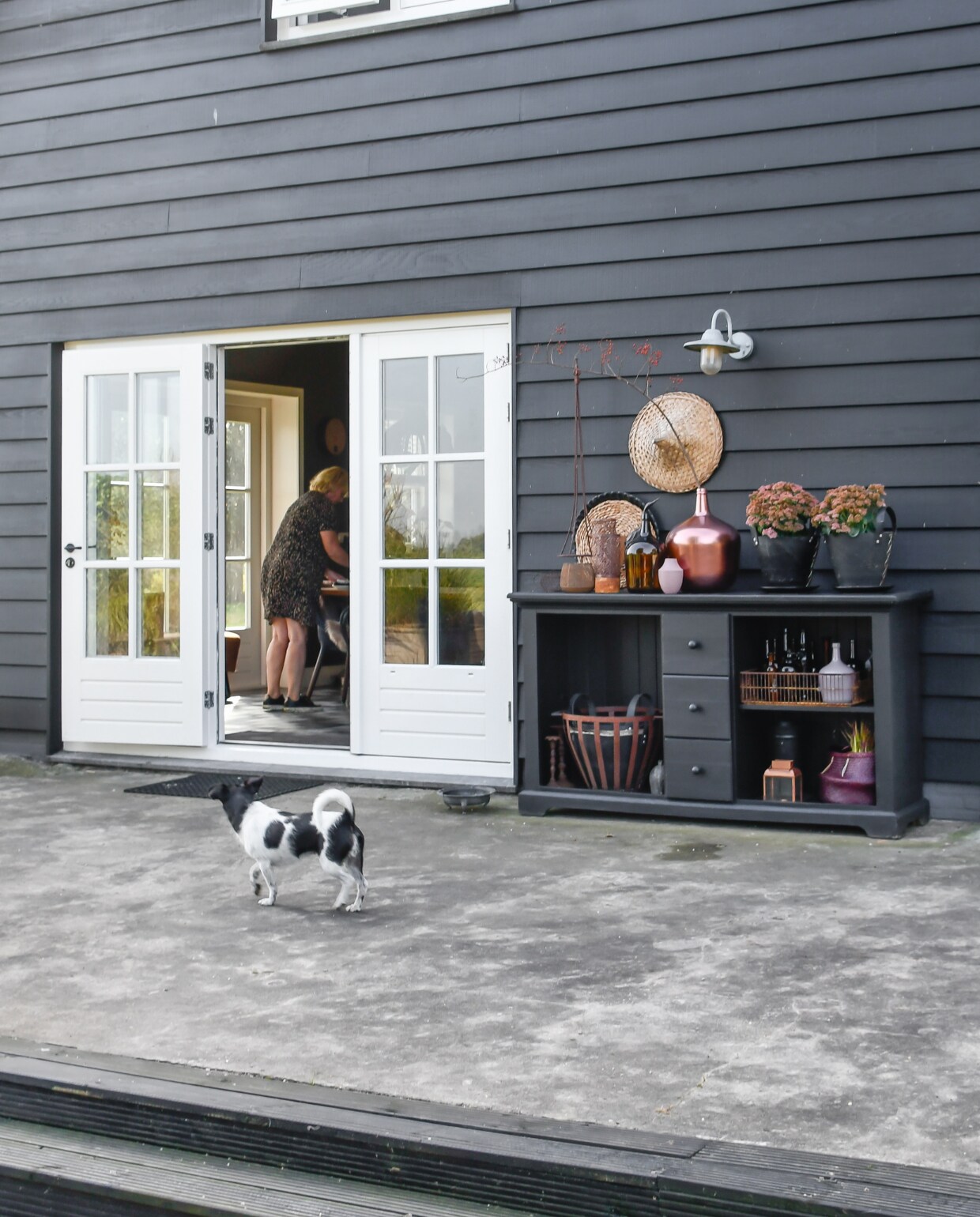 Hond Noortje op de oude vloer van de stal. ‘Daar moet nog wat mee’, vindt Saskia. Voor nu voldoet de vloer, maar echt mooi vindt ze hem niet. Het huis is bekleed met rabatdelen van red ceder, die door Saskia met teerverf zijn geschilderd. Kast gekregen van schoonzus, zelf zwart geschilderd. Hoed kringloop, zwarte manden Loods 5, verroeste boom Pand 96, verroest krat brocante uit Frankrijk. Rest kringloop. vtwonen special tuin 07 | styling Marieke de Geus | fotografie Barbara Groen