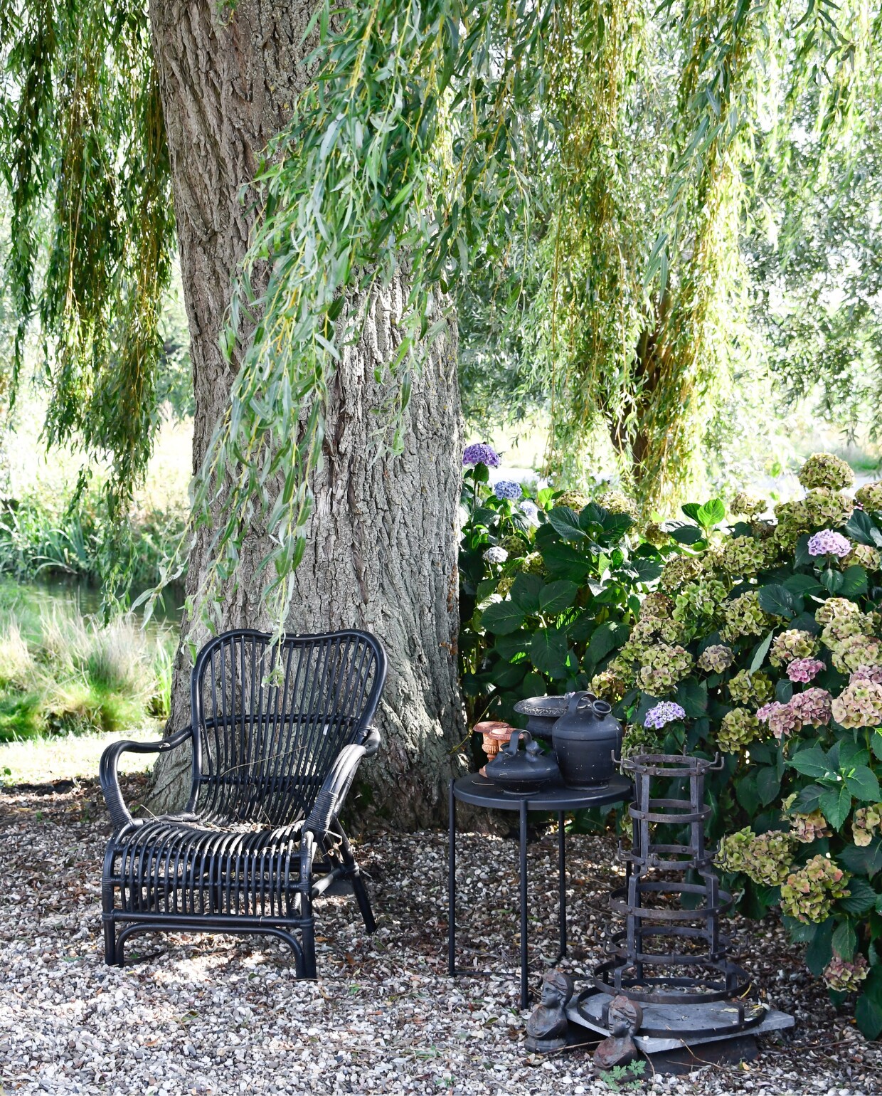 Stoel Jysk, tafel Ikea zelf zwart gespoten, alles erop van de kringloop. Rek rommelmarkt, vrouwtjes onder de steen brocante uit Frankrijk. Onder de treurwilg hortensia’s. vtwonen special tuin 07 | styling Marieke de Geus | fotografie Barbara Groen