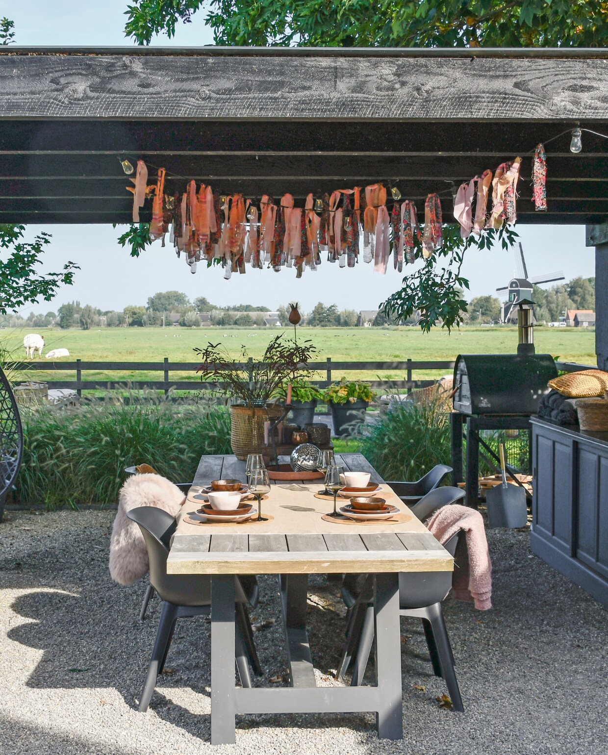 Eettafel Tuinmeubelshop Gouda, stoelen Kwantum. Servies Hema, glazen en bestek H&amp;M Home, placemats bol.com, vacht Ikea, kleed Kwantum, discobol kringloop, mand Kwantum, kaarsenstandaard en verroest tafeltje met waxinelichtjes Loods 5. Rechts een oude duiventil, gekregen van een buurman. Slingers boven tafel zelfgemaakt van stoffen van de kringloop. vtwonen special tuin 07 | styling Marieke de Geus | fotografie Barbara Groen