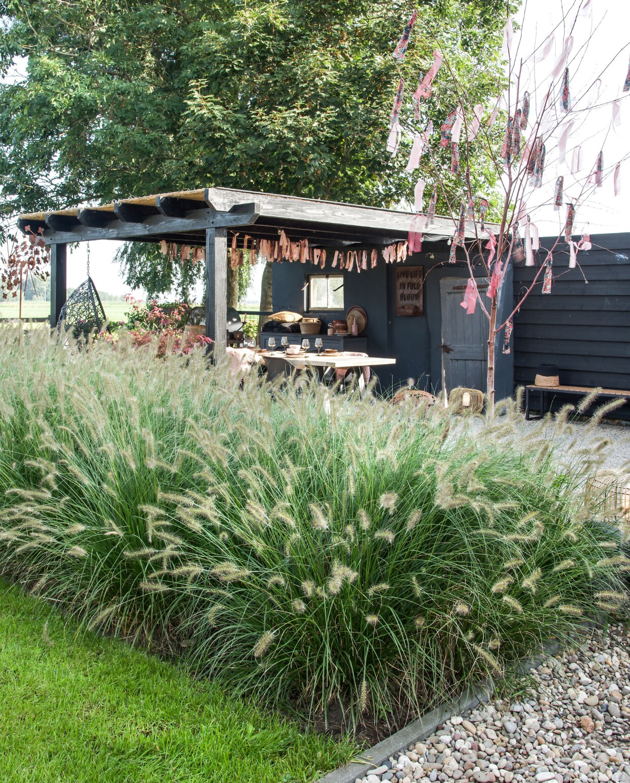 De terrasoverkapping rust op de muur van de oude geitenstal. Eettafel Tuinmeubelshop Gouda, stoelen Kwantum, kastje oude buffetkast, slingers zelfgemaakt. vtwonen special tuin 07 | styling Marieke de Geus | fotografie Barbara Groen