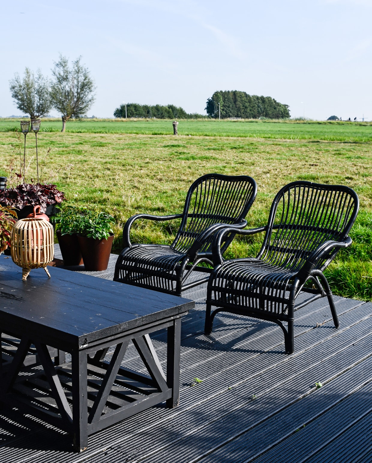 De favoriete plek van Saskia: het terras met uitzicht over het weiland. Vlonders van zwart geschilderd hardhout. Stoelen Jysk. Tafel twee salontafels van Rivièra Maison met een plank erop, zelf zwart geschilderd. Lantaarn kringloop. vtwonen special tuin 07 | styling Marieke de Geus | fotografie Barbara Groen