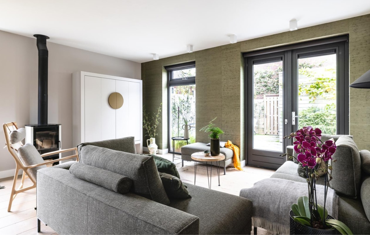 Flexa Creations muurverf kleur Urban Taupe (flexa). Behang Natural Wallcoverings 3 / 303514 prijs op aanvraag (eijffinger.com). Raambekleding Rollerblinds Linbo 08-08-100 L 100 prijs op aanvraag (woninginrichting-aanhuis.nl). DIY: moderne Chinese bruids/tv-kast prijs op aanvraag (remmers-design.nl), geschilderd in Flexa Creations kleur Urban Taupe en handvat in kleur Autumn Gold (flexa.nl). Ingebouwde led-strip prijs op aanvraag (remmers-design.nl). Hoekbank Aikon Lounge van Design on Stock vanaf € 3398,-, fauteuil Dedo van Gazzda € 1540,-, vloerlamp Triangle van HKliving € 269,-, vloerkleed Hem van Ferm Living € 585,- (eijerkamp.nl). Plantentafel € 74,99 (micadecorations.nl). Op zwart tafeltje (privébezit) zwarte kandelaar Hoy Casted van Ferm Living € 79,-, vaas Anse van Ferm Living € 119,-, naast tv-kast handgeschilderde vaas van Return to Sender € 162,95, plaid van Silkeborg Fanø € 119,99 (vtwonen.be). Overig privébezit. vtwonen weer verliefd op je huis seizoen 15 aflevering 8: Heiloo | Styling Frans Uyterlinde | Fotografie Sonja Velda
