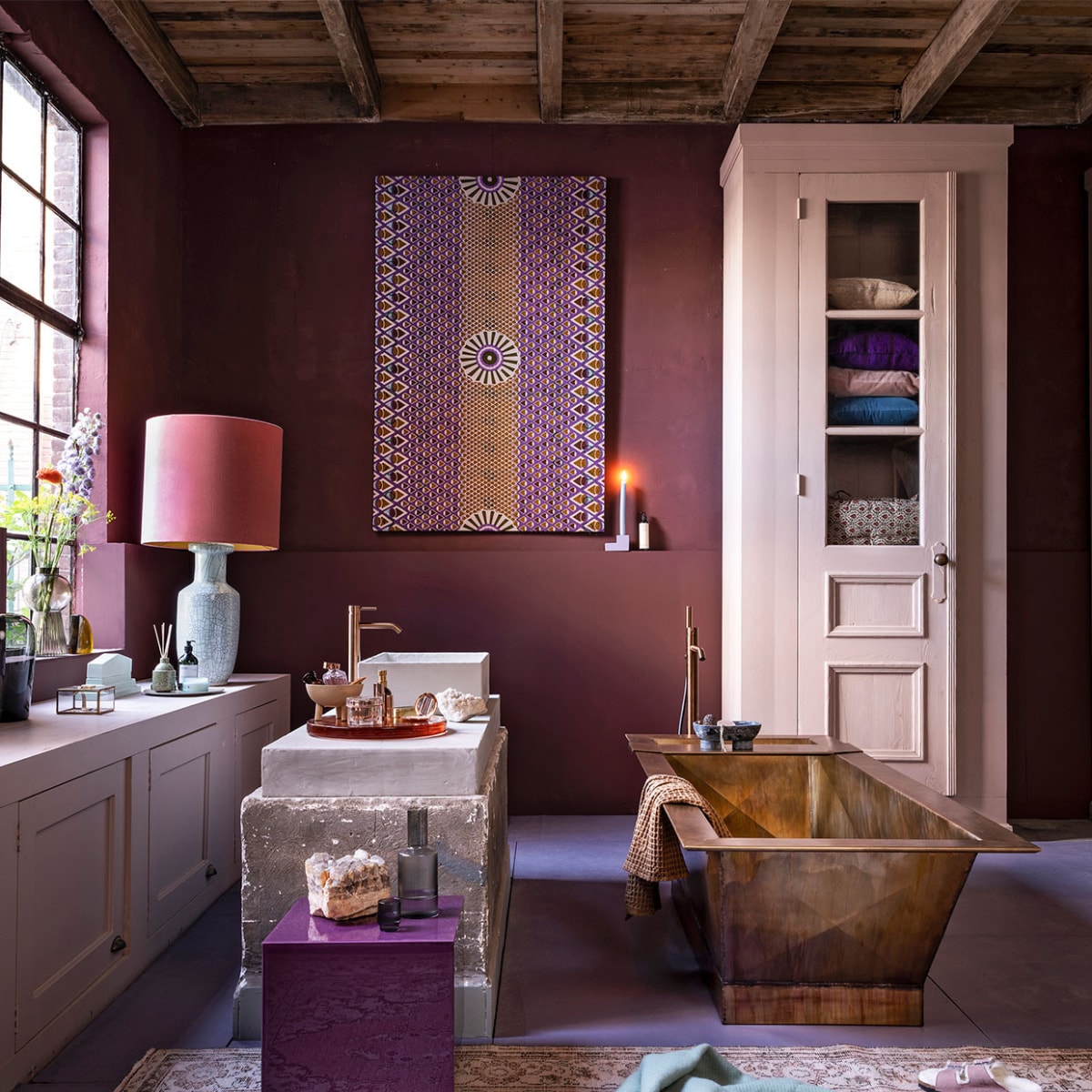 Badkamer aubergine , , Op de muur krijtverf Moorland per liter € 39,30, op de vloer lakverf Bohemian per liter € 61,40, verf op de kasten lakverf Old Rose per liter € 61,40 (pure-original.nl). Kasten, beide op maat gemaakt, prijs op aanvraag, wasbak prijs op aanvraag (com-anders.nl). Bad in gepatineerd messing, 2000x815x555 cm (lxbxh), prijs op aanvraag bij de koperslagerij (juliusballer.nl). Losstaande kraan in brons € 2050,-, wastafelkraanin brons € 525,- (jee-o.com). Plexiglazen tafel van HKliving € 195,- (vtwonen.be). Doek van waxstof item nr. VL40850.365.02 vanaf € 54,95 (vlisco.com). Vloerkleed € 495,- (rozenkelim.nl). Lampenkap € 375,-, lampenvoet € 396,- (polspotten.nl). Glazen vaas van Menu € 69,95, glazen vaas op vensterbank van Bloomingville € 38,99, bord van HKliving € 17,50, waterkan van Ferm Living € 35,-, glazen van Ferm Living per 4 € 35,-, stenen zeepbakje van Ferm Living € 119,-, wafel handdoek van Ferm Living € 39,- (vtwonen.be). Geel glazen object kwart cirkel van HKliving € 59,95 (deens.nl). Mintgroen keramisch object € 69,95, geurstokjes € 26,95, oranje glazen plateau € 259,- (hkliving.nl). Sieradendoosje € 19,-, kandelaar € 19,95, wollen deken van Hay € 75,- (eijerkamp.nl). Schaaltje op 3 poten € 30,- (101cph.com). Overig privébezit. vtwonen 10-2020 | styling Marianne Luning | fotografie Stan Koolen