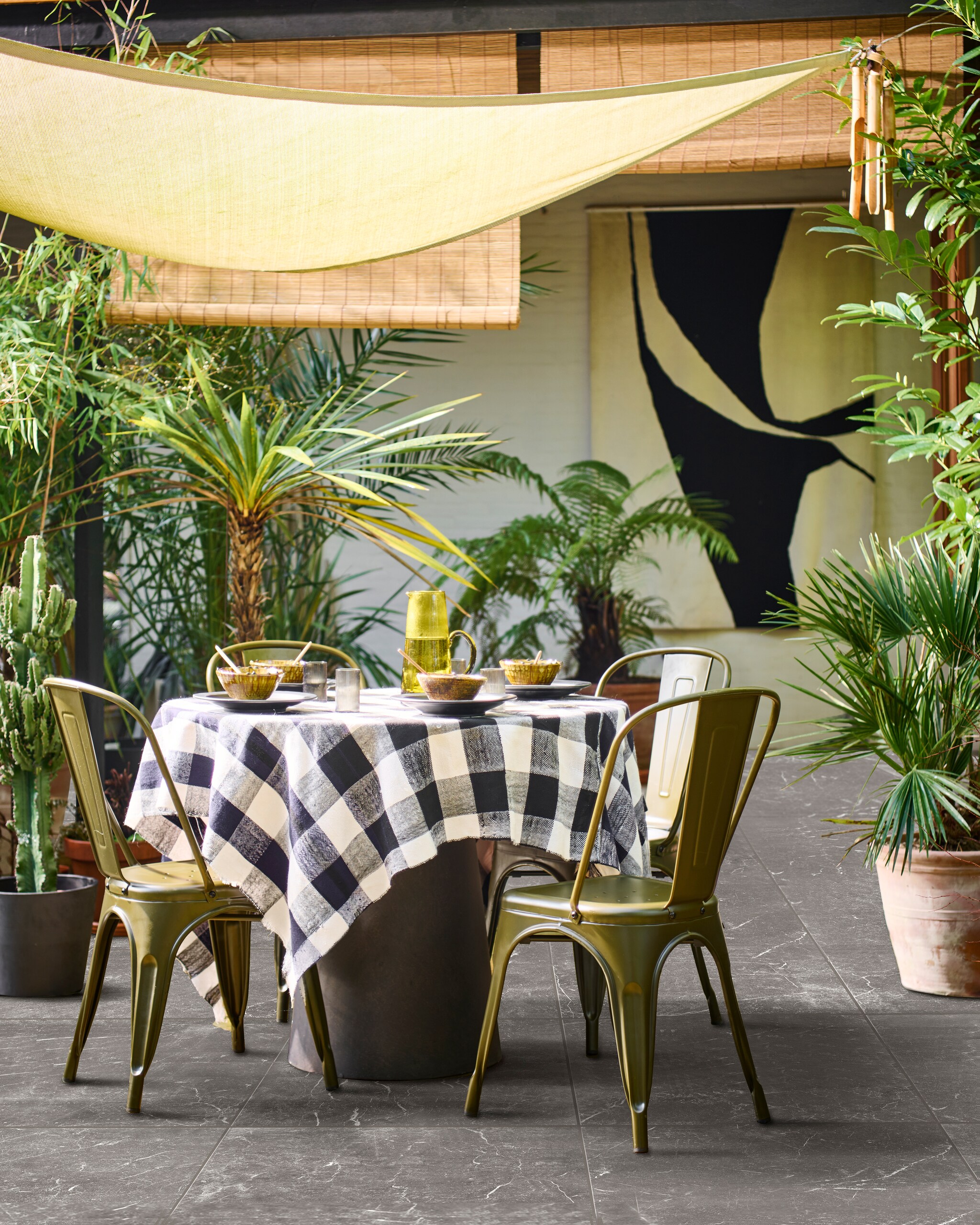 Eetkamerstoel Afternoon in camouflage groen, 53x44x85 cm (bxdxh) € 99,95. Tuintegel Solostone Outside Marble, 90x90 cm per m² € 89,50.M.m.v. basiclabel.nl (ronde betonlook eettafel Damon), householdhardware.nl (zwarte borden, okergele Tamegroute kommen, houten lepels, olijfgroene glazen kan, tafelkleed), vtwonen.nl (waterglazen van Ferm Living, grijze bloempot). Overig privébezit. vtwonen 04-2023 | productie Tanja Saarberg | styling Marlies Does | fotografie Sjoerd Eickmans