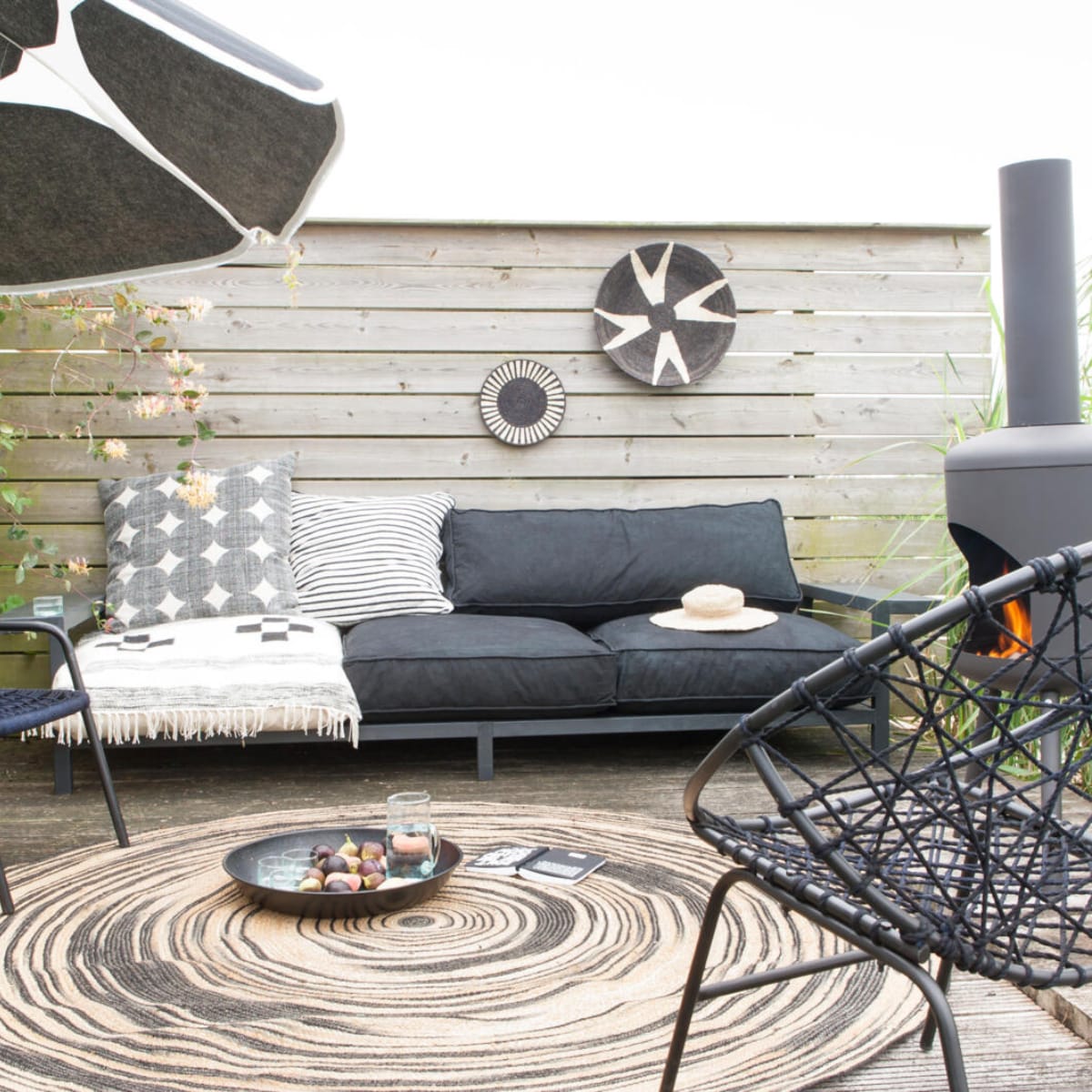 Houten bank met brede armleuningen vanaf € 375,- (Combitex). Zwarte draadstoelen links € 165,- rechts € 299,- (Madam Stoltz). Rond vloerkleed van HK Living, Ø 200 cm € 199,-, terrashaard van RedFire BonFeu € 89,- (www.vtwonen.nl). Rotan kruk van Madam Stoltz, set van 2 € 107,- (www.deens.nl). Outdoor matraskussens, vanaf 80x80x15 cm (bxlxh) € 169,-, rubberen mand € 25,50, gestreepte mok € 9,75, glazen kan € 15,50 (Household Hardware). Kussen met cirkels € 59,- (Sissy-Boy). Jersey kussen met strepen € 69,95 (www.10days.nl). Rechthoekig kussen € 120,- (Trendhopper). Sisal borden vanaf € 29,- (Couleur Locale). Parasolstof met  stippen Kivet per meter € 43,- (Marimekko). Overig privébezit. vtwonen 05-2017 | Styling Marianne Luning | Fotografie Anna de Leeuw
