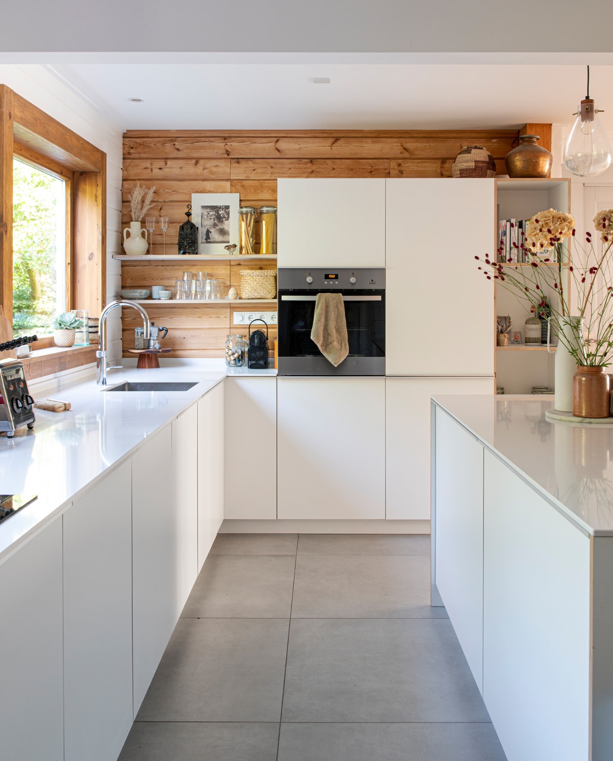 Vloertegels Tegels in Huis, keuken eigen ontwerp. Op de planken: kruikvaas van Ibiza, windlicht en zwart-witfoto uit Marokko, spaghettipotten Ikea, servies uit Japan, picardieglazen van Duralex, wijnglazen Cin in Wonen, mand Dille &amp; Kamille. Taartplateau H&amp;M Home, koffiezetter Bialetti, koffieapparaat Nespresso, oven Zanussi, mand uit Ibiza, bronzen waterkruik uit India. Overig onbekend. vtwonen 04-2023 | productie De Binnenkijkers | styling Jeske Weel | fotografie Caroline Coehorst