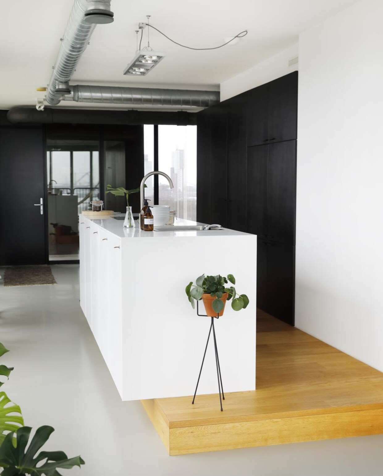 Het witte keukenblok, een ontwerp van Martin, is gemaakt van Corian. De zwarte kast is ook door Martin ontworpen en loopt de hoek om door naar het eetgedeelte. Lamp Rietveld Licht. Witte plantenpot Habitat. Op het aanrecht: glazen vaasje Serax. Bruin flesje waar Leanne een zelfontworpen etiket op heeft geplakt. Witte schaaltjes Ikea. Erachter een weckpot van Cook &amp; Co. Plantenhouder Ferm Living. Rechts grijze kist Loods 5. vtwonen 05-2018 | fotografie &amp; Styling Peggy Janssen