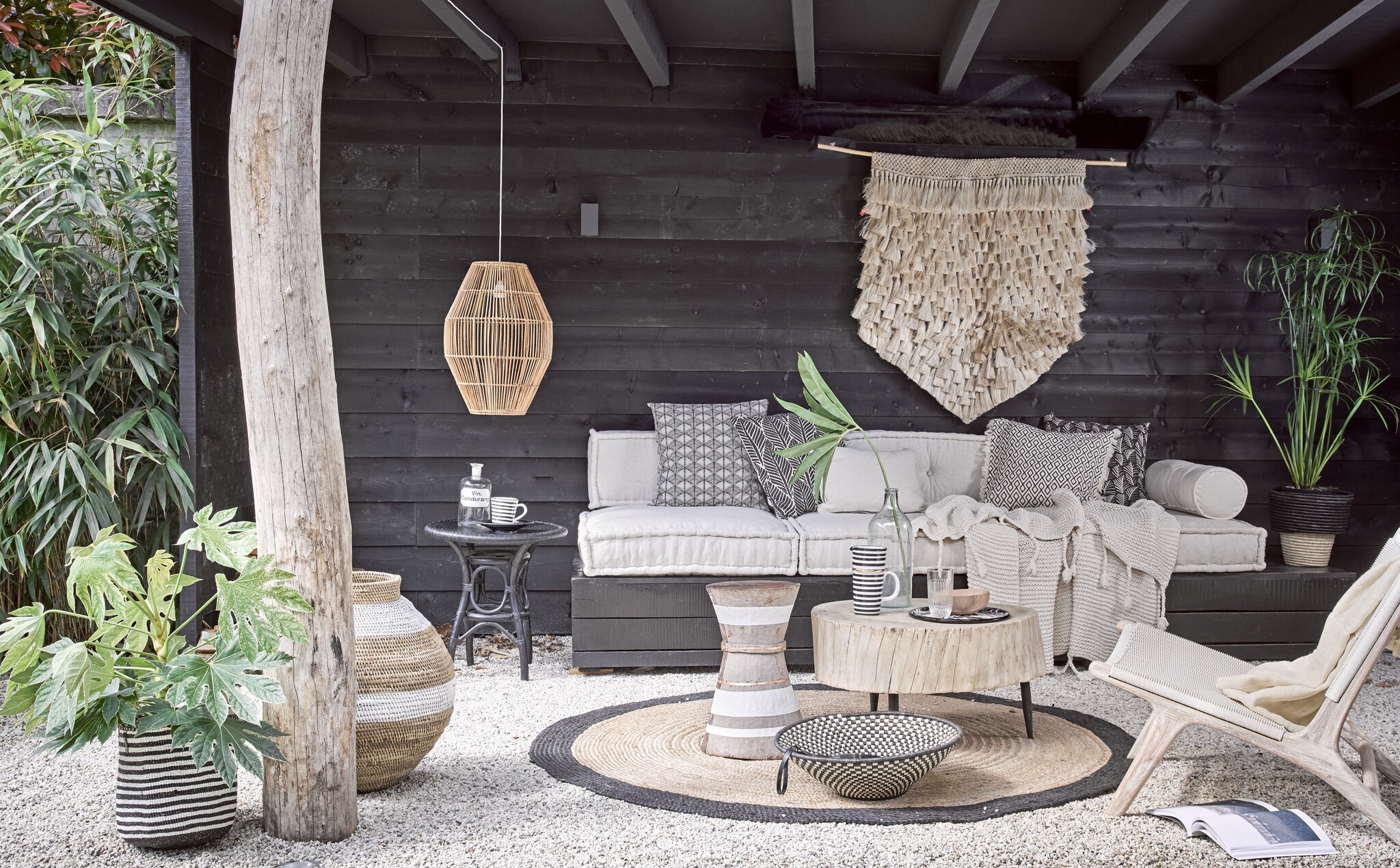 Loungekussens 80x80x15 cm, rugkussen 120x30x15 cm, rolkussenhoes, ecru kussen 50x50 cm (Household Hardware). Wandkleed, houten buitenstoel, hoge gevlochten pot met witte band, houten bijzettafel met witte bies, grote houten tafel, lage schaal in zwart-wit, hanglamp, zwart-wit gestreepte mand, gevlochten pot met zwarte rand, ecru plaid Kaldi op stoel (Couleur Locale). Gebreide deken, vloerkleed rond 180 cm (Madam Stoltz). Emaillen dienblad (WolfWare). Hoge gestreepte kan, gestreepte beker (Maison NL). Houten kom (HK Living). Glas (Six and Sons). Oude apothekersfles (De Weldaad). Glazen fles (Burbri Antiek). Zwarte bijzettafel (All the Luck in the World). Gedessineerde kussenhoes links, kussenhoes met zwarte bladeren, kussenhoes met rafels en grafisch dessin, zwarte kussenhoes met witte blaadjes (H&amp;M Home). vtwonen 2017-08 | styling Cleo Scheulderman | fotografie Alexander van Berge