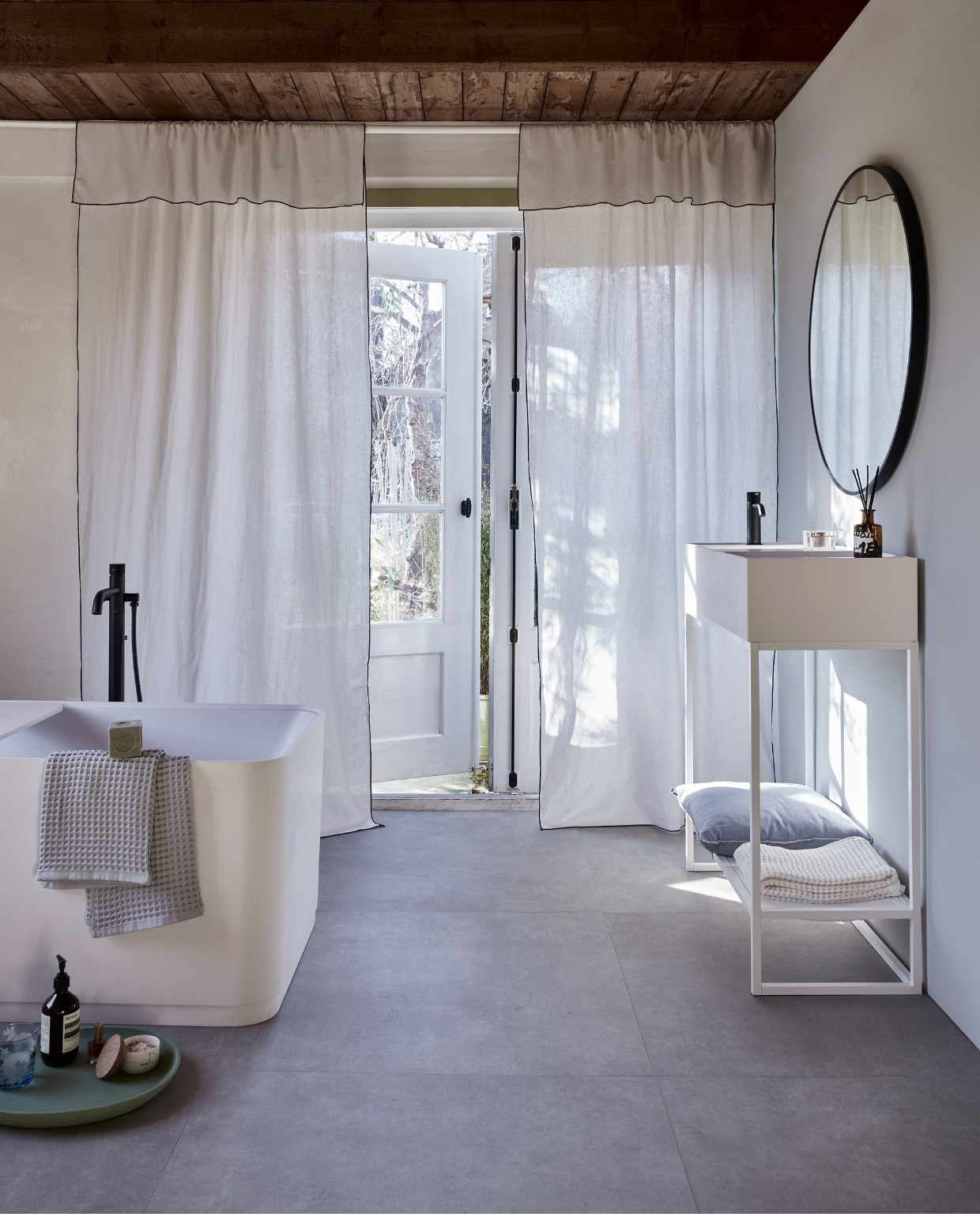 Witte gordijnen met zwarte rand, linnen en katoen, 120x250 cm (bxh), set van 2 € 59,99 (hm.com). Uitschuifbare gordijnroede Hugad, 210-385 cm (l) € 12,99,- en uitschuifbare gordijnroede Räcka, 210-385 cm (l) € 9,99,-, aan elkaar gedraaid (ikea.nl). Muurverf Tin van vtwonen, per liter € 27,99 (karwei.nl). Lichtgrijze pvc-vloer Basic XL van vtwonen, dryback, per m2 € 67,95 (vtwonen). Kussen Outline in Ice Blue van Hay, katoen en linnen € 85,- (vtwonen.be/shop). Bad Soft Edge van vtwonen, 160x73x59,5 cm (lxbxh) € 4400,-, waskom van vtwonen € 869,-, wastafelmeubel met inlegblad van No Limit € 847,-, spiegel, 90 cm (Ø) € 431,- (detremmerie.be). Wastafelmengkraan Roma € 369,-, vrijstaande badkraan Roma € 1829,- (plieger.nl). Wafelhanddoeken € 65,- (hay.nl). Groen dienblad, set van 3 € 175,-(polspotten.nl). vtwonen 05-2023 | styling Marianne Luning | fotografie Alexander van Berge