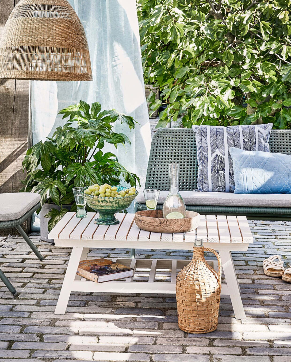 Bank Wivinia € 419,- en stoel Wivinia € 211,50 van Kave Home (vtwonen.nl). Gordijn gemaakt van linnen stof per meter € 25,- (ochreandred.nl). Kussen met print Heringbone € 25,95, lichtblauw kussen Naida € 19,99 (intratuin.nl). Schaal op voet € 99,95, walnoothouten schaal € 75,-, glazen karaf Cigogne € 23,50, glazen op voet Diabolo per stuk € 6,80 (householdhardware.nl). Instappers € 35,99 (zarahome.com). Rieten lamp Torared € 39,95 (ikea.com). Plaid Native Fan € 34,99 (sissy-boy.com). Sisal kussen € 25,- (loods5.nl). Overig privébezit. vtwonen tuin special 4-2021 | productie Corrien Flohil | uitvoering Johan Snoodijk @snoodijkencostyling Moniek Visser | fotografie Peggy Janssen