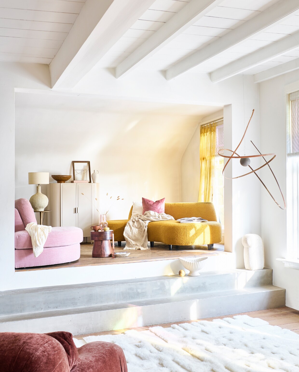 Okergele bouclé bank Organic, 214x91/174x74 cm (bxdxh) € 1419,-, beige metalen muurkast Montrela, 100x42x114 cm (bxdxh) € 1195,-, wit wollen vloerkleed, 190x290 cm € 989,-, bruine papier-maché schaal € 29,95, witte keramieken vaas op kast, 14x11x25 cm € 29,95, roze fluwelen kussen, 50x50 cm € 44,95, wit linnen kussen, 50x50 cm € 45,-, beige plaids van katoen en linnen, 140x180 cm per stuk € 49,95, natuurstenen schaaltje € 65,-, roze glazen vaas € 27,95, roze glazen kandelaar € 12,95 (hetkabinet.nl). Roze 1-zits element Family van vtwonen, 93x98x85 cm (bxdxh) € 629,-, messing bijzettafel van Moos, 35x65 cm (Øxh) € 130,99, porseleinen schaal op voet van Ferm Living, 13,7x7,3 cm (Øxh) € 199,-, (vtwonen.nl/shop). Mangohouten kruk Tak, 39x34 cm (Øxh) € 149,-, beige papier-maché lampvoet van BePureHome, 35x53 cm (Øxh) € 149,- (basiclabel.nl). Bank op voorgrond Divano Lounge in Vintage Brick, 300x113x83 cm (bxdxh) € 3995,- (hkliving.com). Houten bal € 5,-, oud glazen bakje € 9,- (jolandelijk.nl). Gordijn Flat Yellow Mellow van Numero 74, 100x290 cm (bxh) € 54,- (lidor.nl). Overig privébezit. vtwonen 05-2023 | styling Marlies Does | fotografie Sjoerd Eickmans