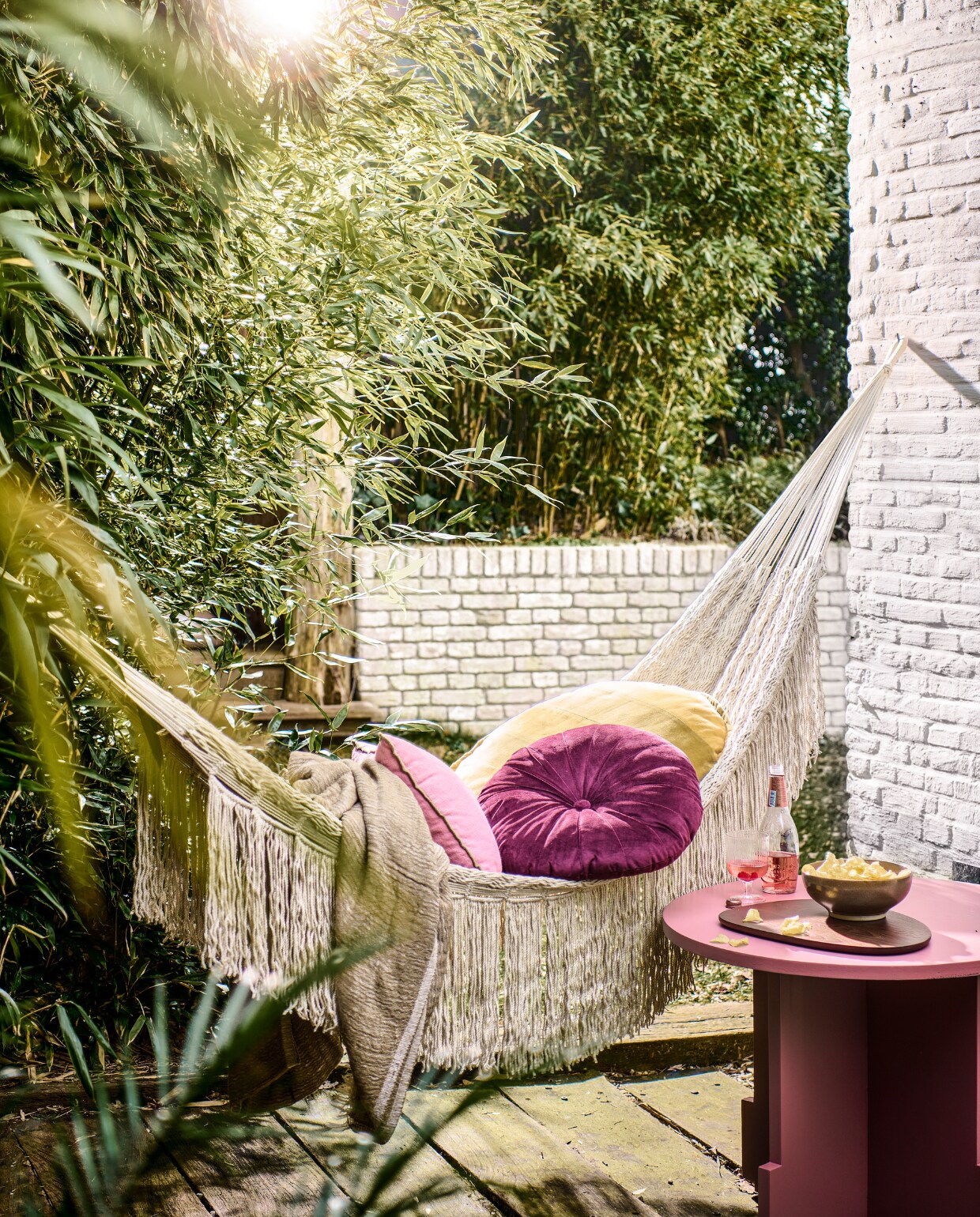 Ecru hangmat van Ferm Living, 140x320 cm (bxl) € 229,-, keramieken schaal van Ferm Living, set van 3 € 79,-, plaid van House Doctor € 98,10 (deens). Paars fluwelen kussen, 34 cm (Ø) € 34,95, houten snijplank Cairn van Ferm Living, set van 3 € 135,- (vtwonen.be/shop). Ronde houten tafel, geschilderd in kleur Adventurer van Little Greene, prijs op aanvraag (com-anders.nl). Geel gestreept kussen € 69,95, roze linnen kussen € 37,76 (hkliving.com). Overig privébezit. vtwonen 05-2023 | styling Marlies Does | fotografie Sjoerd Eickmans | assistentie Mandy Kimmijzer