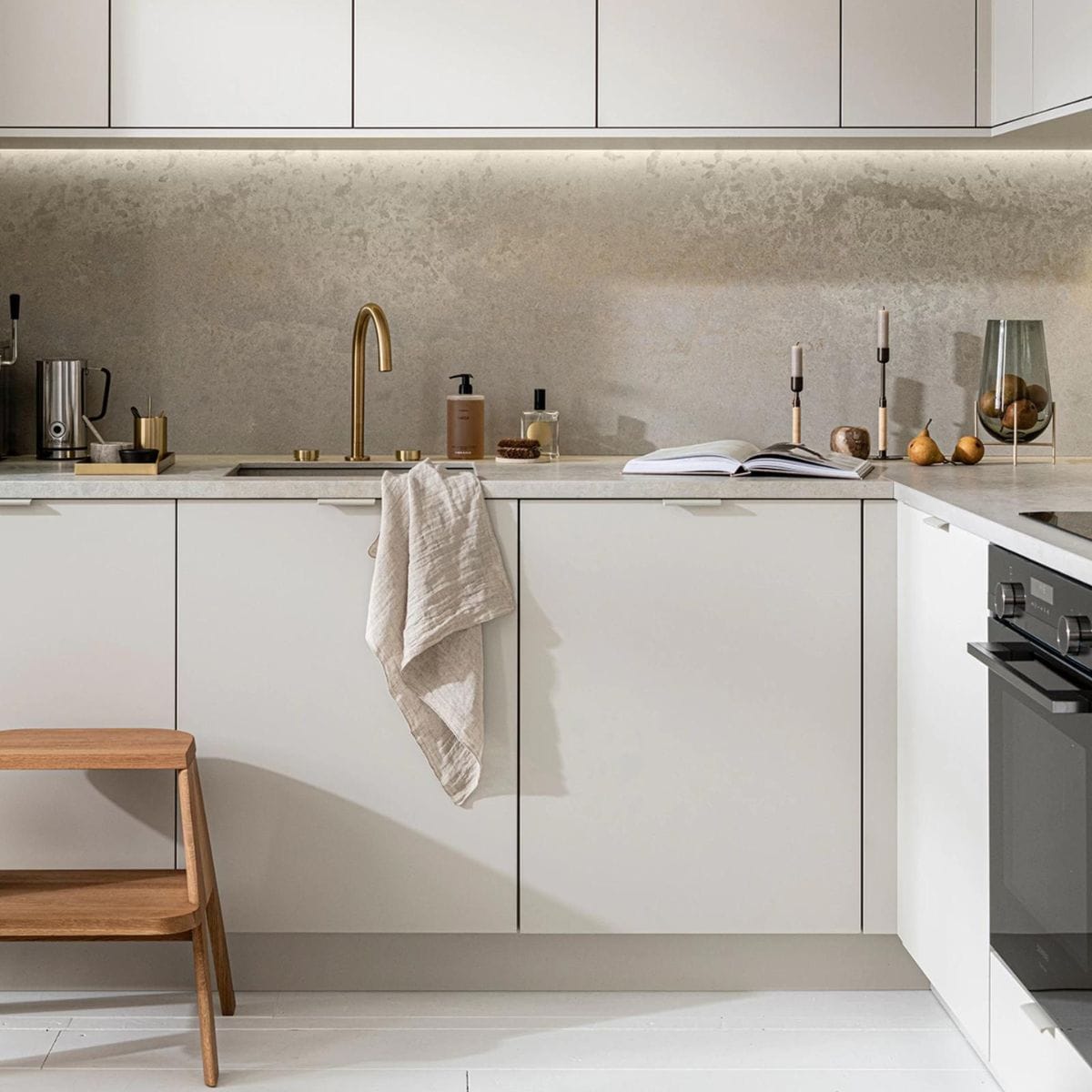 Keuken Basic Greige, vanaf € 21.500,-, M.m.v. thefinestore.com (houten krukje van Hay, messing dienblad en beker van Ferm Living, bronzed brass kandelaren Duca van Menu), flinders.nl (vaas van gerookt glas op messing pootjes van Menu), kikubari.nl (spray van Lingua Planta), vtwonen.be (theedoek uit de vtwonen collectie), skins.nl (handzeep Suede Byredo), sjostrandcoffee.nl (melkschuimer). Overig privébezit. vtwonen 03-2021 | Productie Tanja Saarberg | Styling Kim van Rossenberg | Fotografie Sjoerd Eickmans