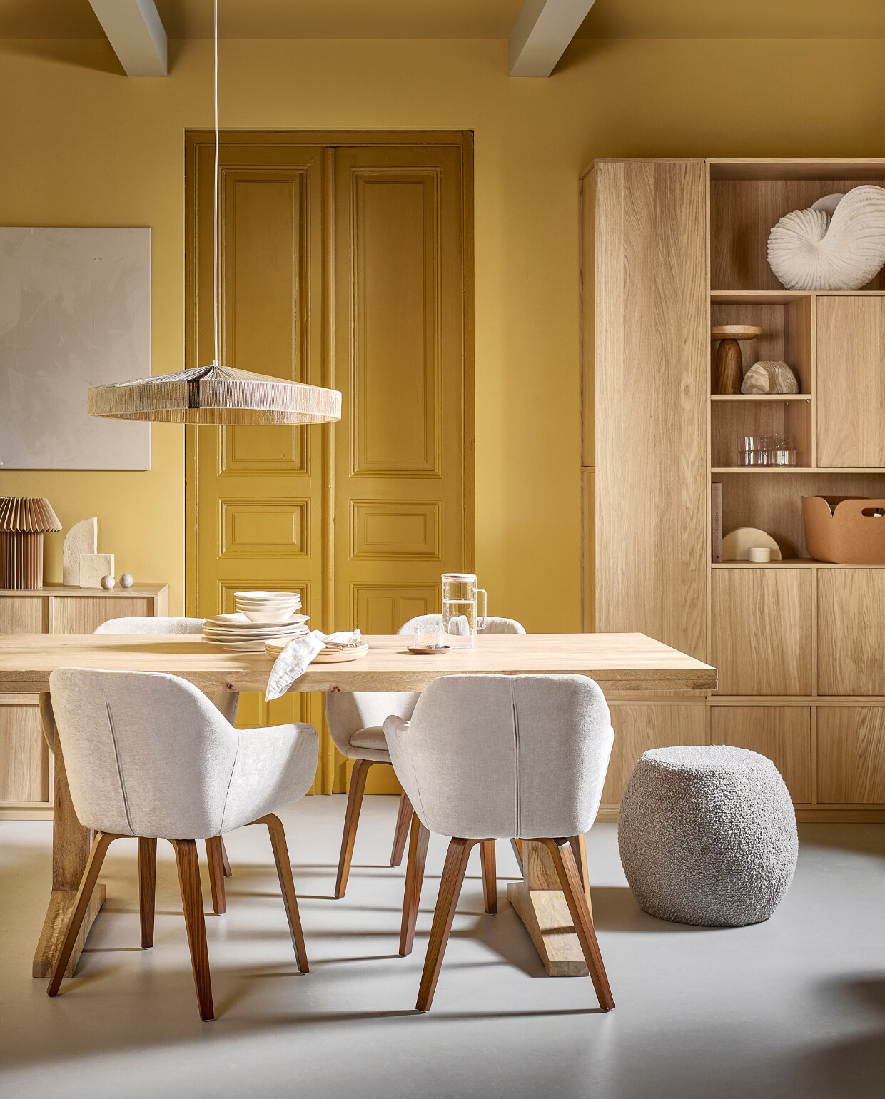 Eetkamerstoelen Base met fluwelen zitting in zand, 58x58x80 cm (bxdxh) € 199,-. Mangohouten eettafel Deck in Naturel, 200x90x78 cm (lxbxh) € 899,-, ook in 120 cm (Ø) in Clay € 749,-. Bouclé poef Soft Bubble in lichtgrijs, 46x45 cm (Øxh) € 119,-, ook in stervorm Soft Star.  Eikenhoutfineer onderkast Modulair, 40x40x44 cm (bxdxh) € 169,-, de Modulair onderkasten zijn verkrijgbaar in breedtes: 40 cm, 77 cm en 110 cm. M.m.v. vtwonen.be/shop (schelpornament van Nordal, opbergmand van Muuto, stenen sculpturen van Ferm Living, muurverf in Straw, lakverf deur in Desert), hm.com (papieren tafellamp), sissy-boy.com (gele aardewerken borden, houten etagère), zarahome.com (aardewerken borden, bestek, linnen servet, glazen karaf met deksel, waterglas, notenhouten onderzetter), flinders.nl (hanglamp Rope van HKliving). Overig privébezit. vtwonen 05-2023 | productie Tanja Taarberg | styling Sanne Ketelaar | fotografie Sjoerd Eickmans