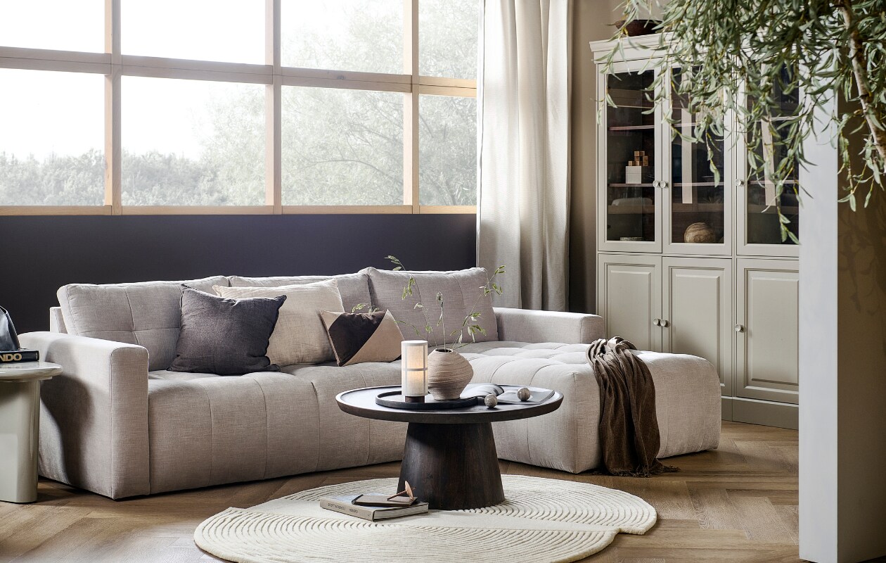 Zetel Bar met chaise longue rechts in zand, 280x170x87 cm (bxdxh) € 1749,-, ook met chaise longue aan de linkerkant en in antraciet, groen, roze en warmgrijs. Grenenhouten vitrinekast Chow 2-deurs in Dakargrau, 54x40x215 cm (bxdxh) € 499,-, ook verkrijgbaar als 4-deurs vitrinekast. Walnotenfineer salontafel Coffee a Gogo, 90x40 cm (Øxh) € 499,-. Mangohouten bijzettafel Beach Small in Clay, 64x51x53 cm (lxbxh) € 319,-, ook in 80x80x41 cm (lxbxh).M.m.v. vtwonen.be/shop (vloerkleed van Bolia, tafellamp van Menu, gestreept kussen van Moos), hm.com (beige aardewerken vaas, bruine plaid), karwei.nl (muurverf Mirre en Warm Brown). Overig privébezit. vtwonen 05-2023 | productie Tanja Taarberg | styling Sanne Ketelaar | fotografie Sjoerd Eickmans