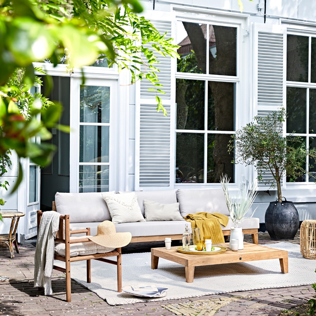Buitentafel MBrace van Dedon 200x90 cm, houten stoelen Tibbo van Dedon (dacks.nl). Witte bistro klapstoelen van Fermob, witte armstoel Luxembourg van Fermob, Serviesgoed uit 12-delige dinner box Nordic Sand van Broste Copenhagen, schaal Nordic Sand van Broste Copenhagen ø 22,5 cm, Serax Surface longdrinkglas Serax Surface 4 stuks, linnen tafelkleed Gracie van Broste Copenhagen 160x300 cm (vtwonen.be). Gele servetten en wit linnen plaid (nordal.eu). Keramieken schaal op klapstoel, linnen lampionnen (sukha.nl). Ladder vanaf (com-anders.nl). Witte vaas (zarahome.com). Stonewashed bestekset Brick Lane 39-delig (luxerybynature.nl). Glazen kan (weldaad.com). Klapkruk van mangohout (hm.com). Okergeel kussen (madamstoltz.dk). vtwonen 07-2020 | Styling Cleo Scheulderman | fotografie Jeroen van der Spek
